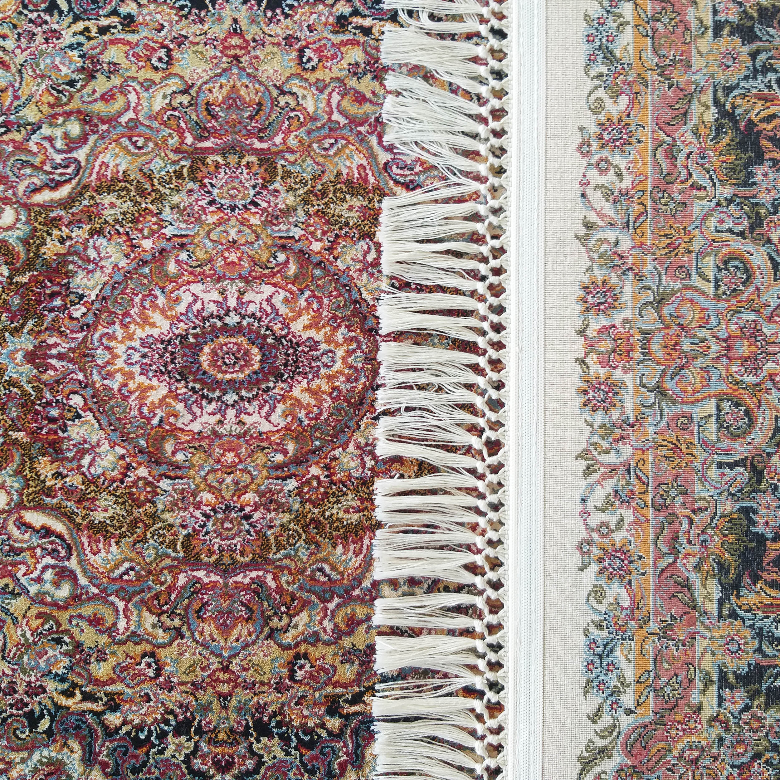 Tapis orné de motifs floraux multicolores avec un médaillon central, bordé de franges blanches et d'une bande claire décorée