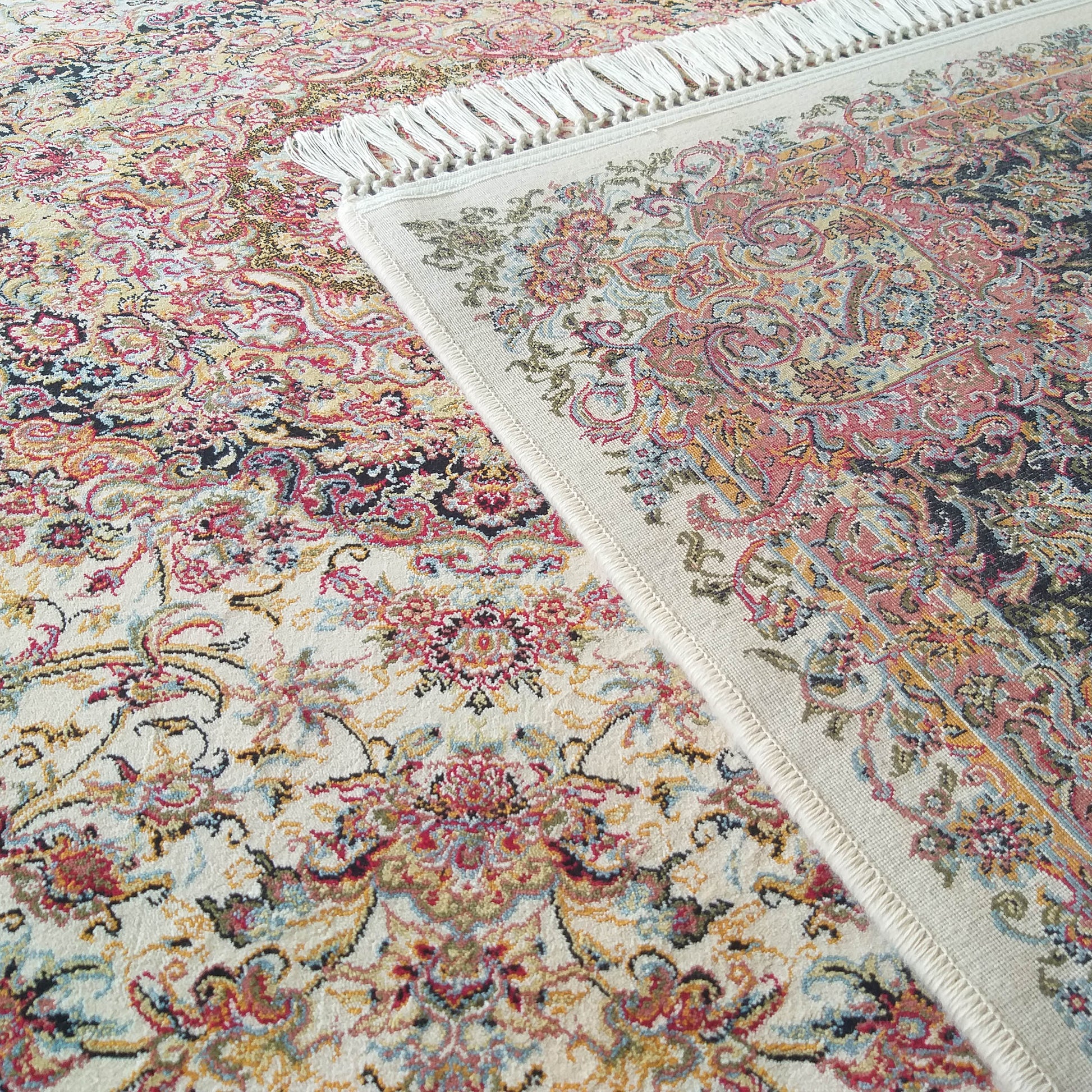 Tapis à motifs floraux et cachemire multicolores (rouge, bleu, or, noir) sur fond crème, avec des franges blanches apparentes