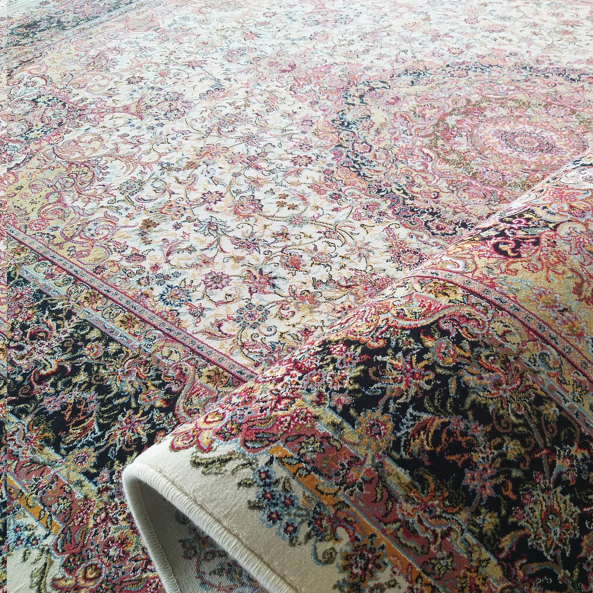 Tapis richement orné de motifs floraux et arabesques multicolores sur fond crème, une section sombre et roulée visible