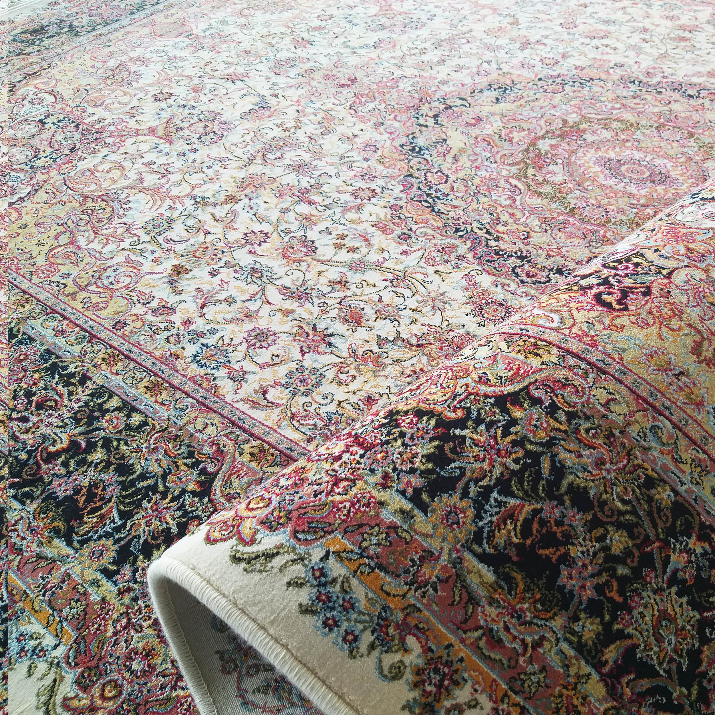Tapis richement orné de motifs floraux et arabesques multicolores sur fond crème, une section sombre et roulée visible