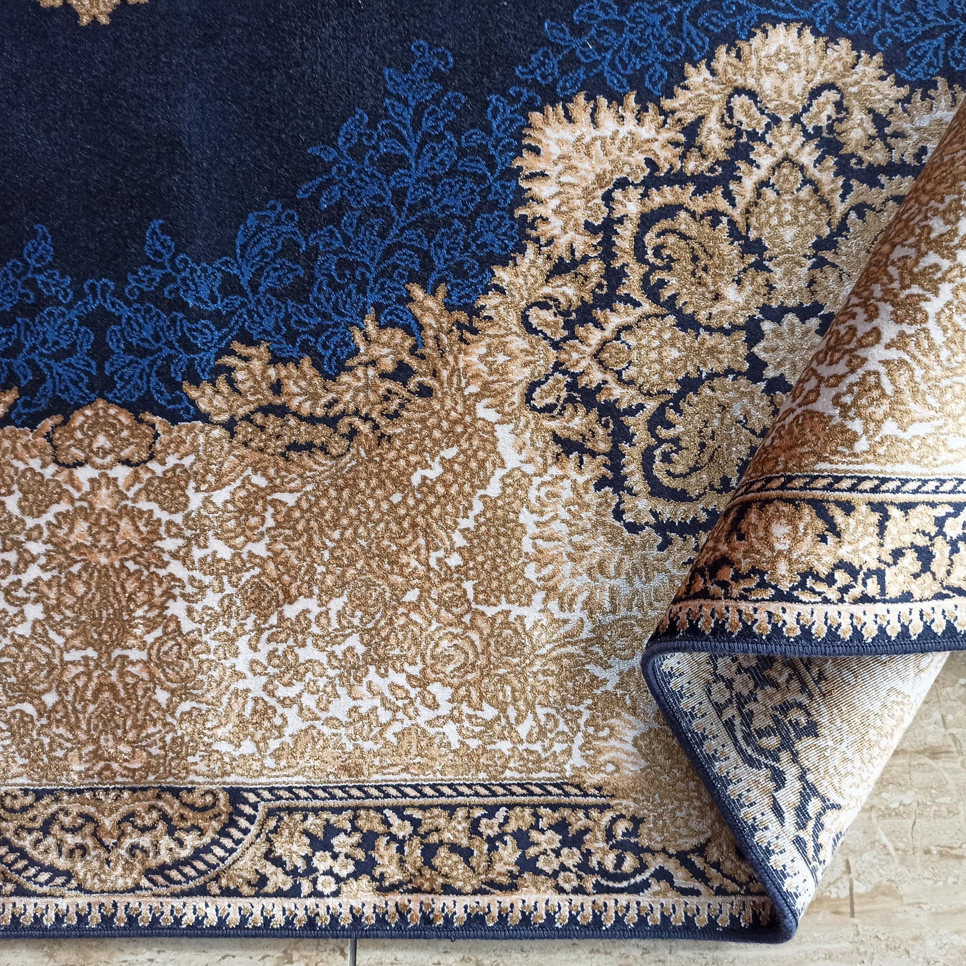 Tapis à motifs ornementaux floraux dorés, bleus et crèmes sur fond bleu foncé, avec une bordure décorée
