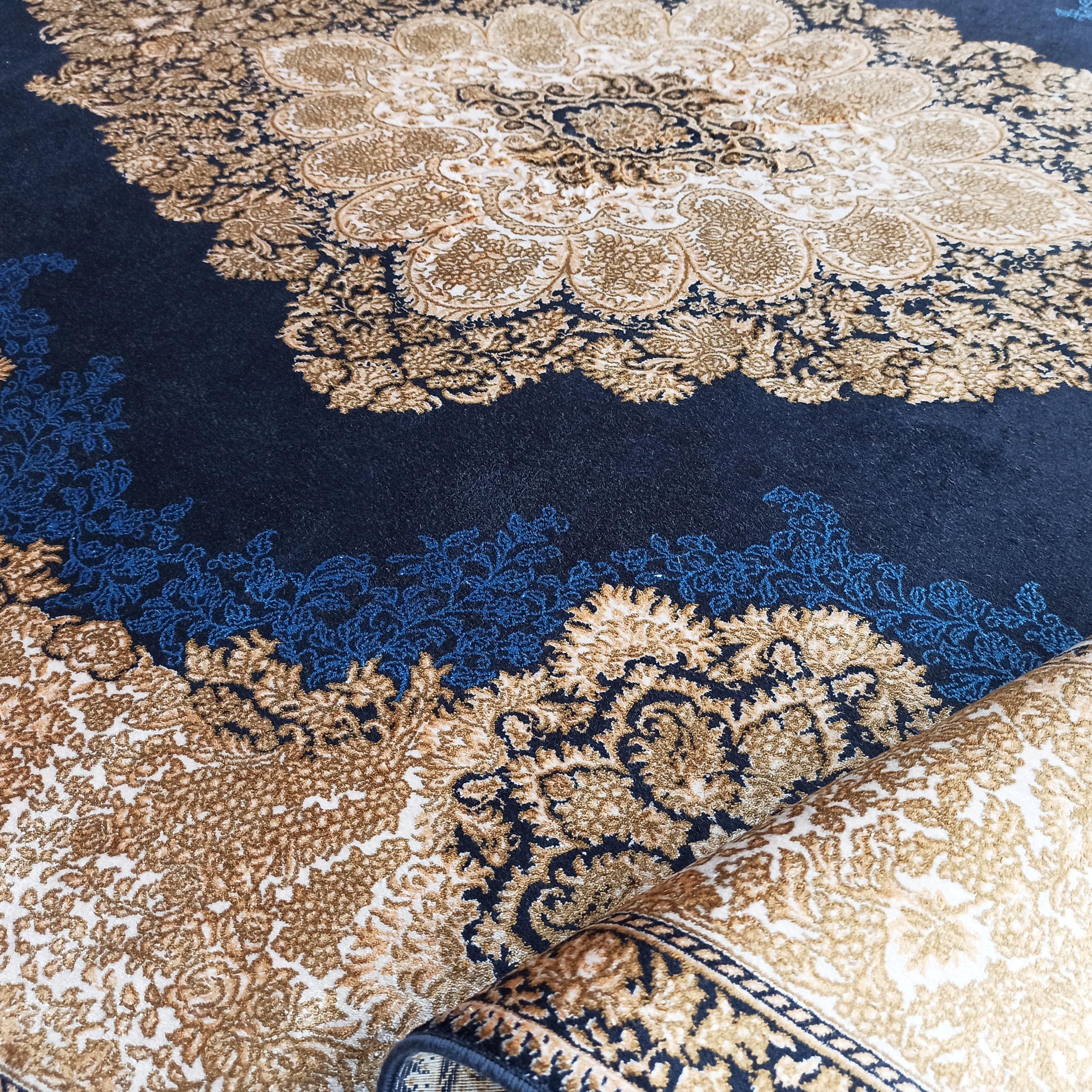 Tapis textile doux bleu nuit avec d'intricats motifs floraux dorés et beiges, une partie du tapis est roulée