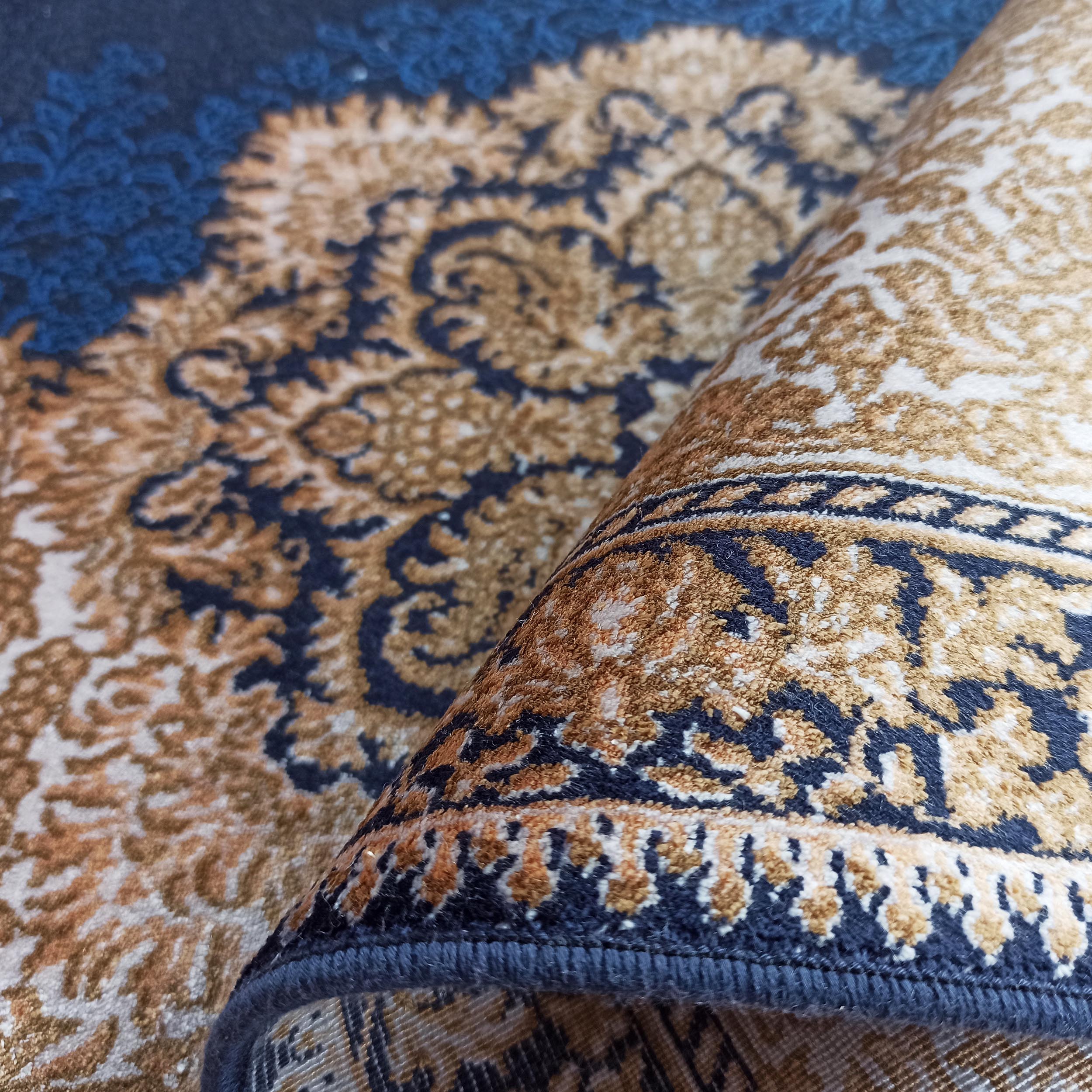 Tapis partiellement roulé aux motifs ornementaux bleu marine, or et crème, avec une texture épaisse et moelleuse