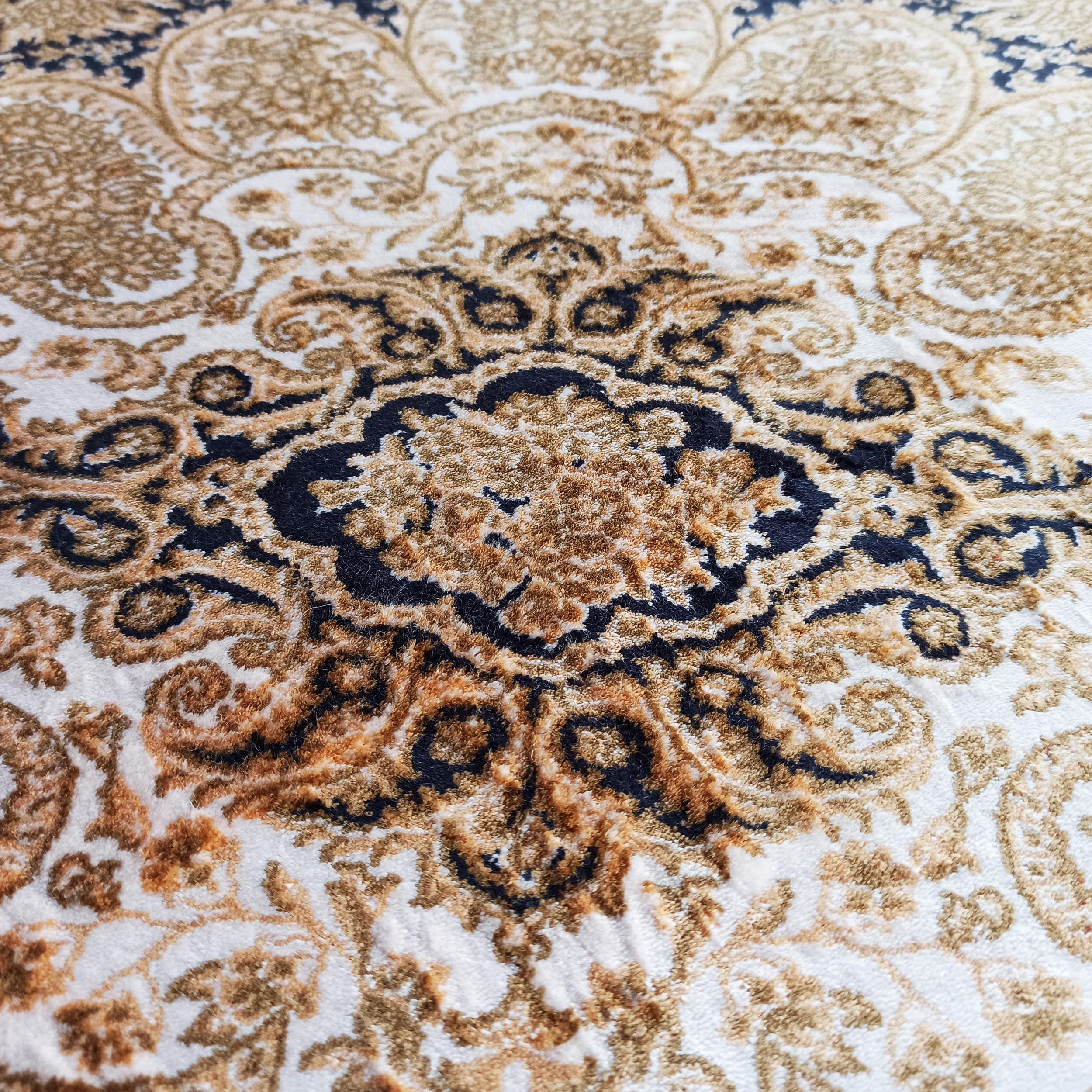 Gros plan sur un tapis texturé aux motifs baroques complexes, mélangeant des tons crème, dorés et bleu nuit