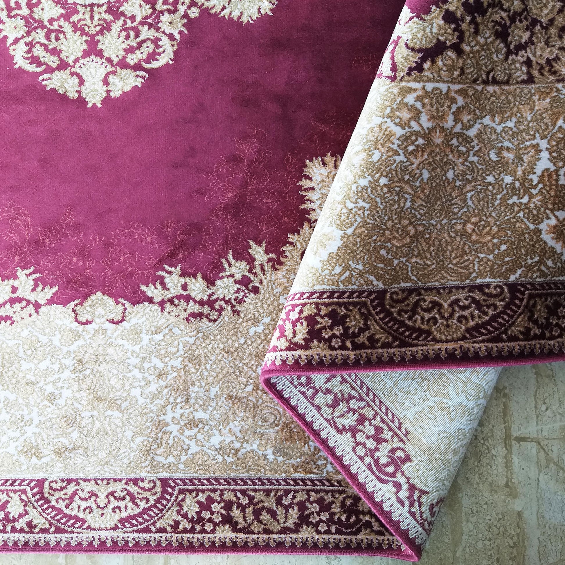 Tapis velouté magenta et beige clair avec des motifs damassés complexes, partiellement enroulé montrant ses bordures