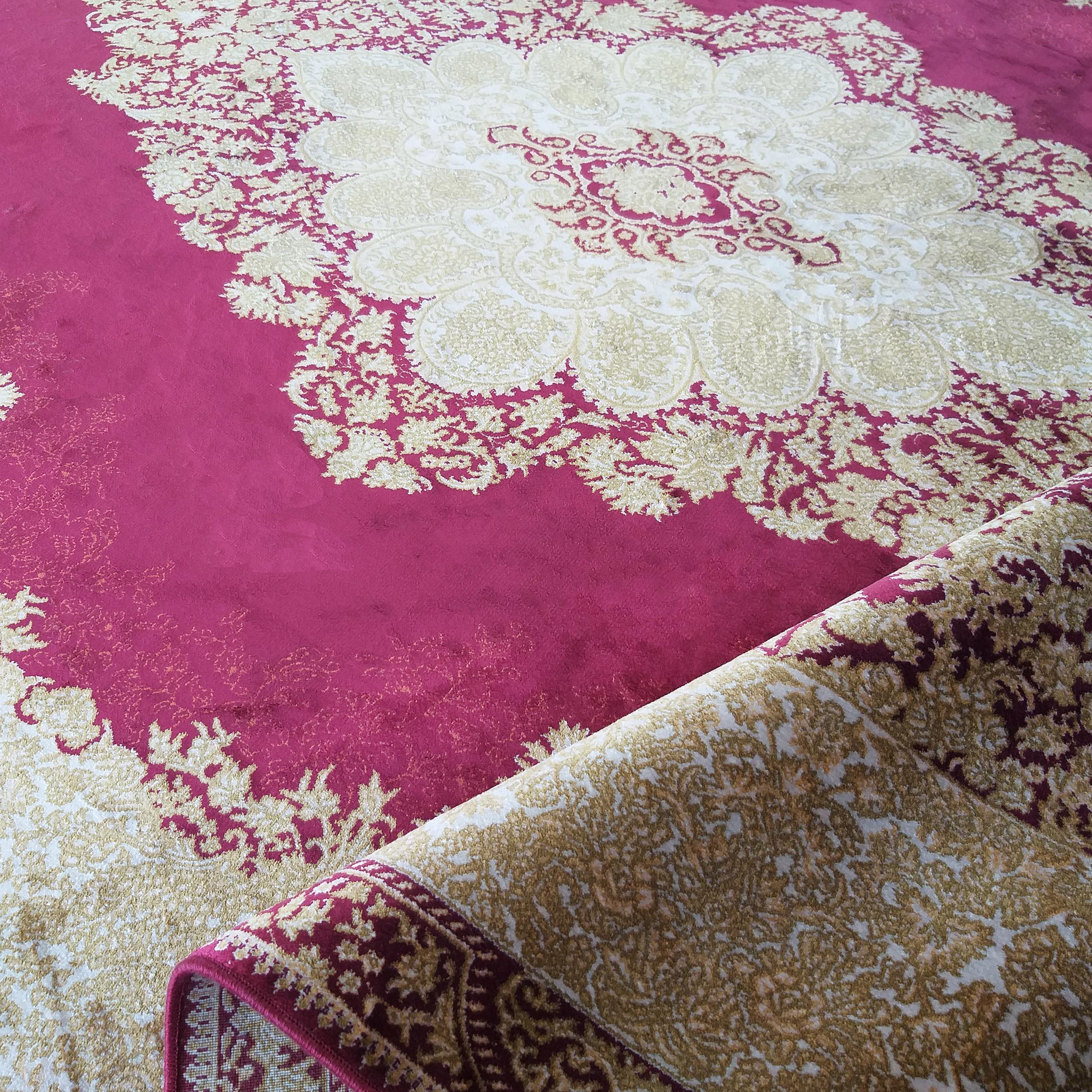 Tapis magenta et beige doré, à motifs floraux et arabesques, partiellement roulé