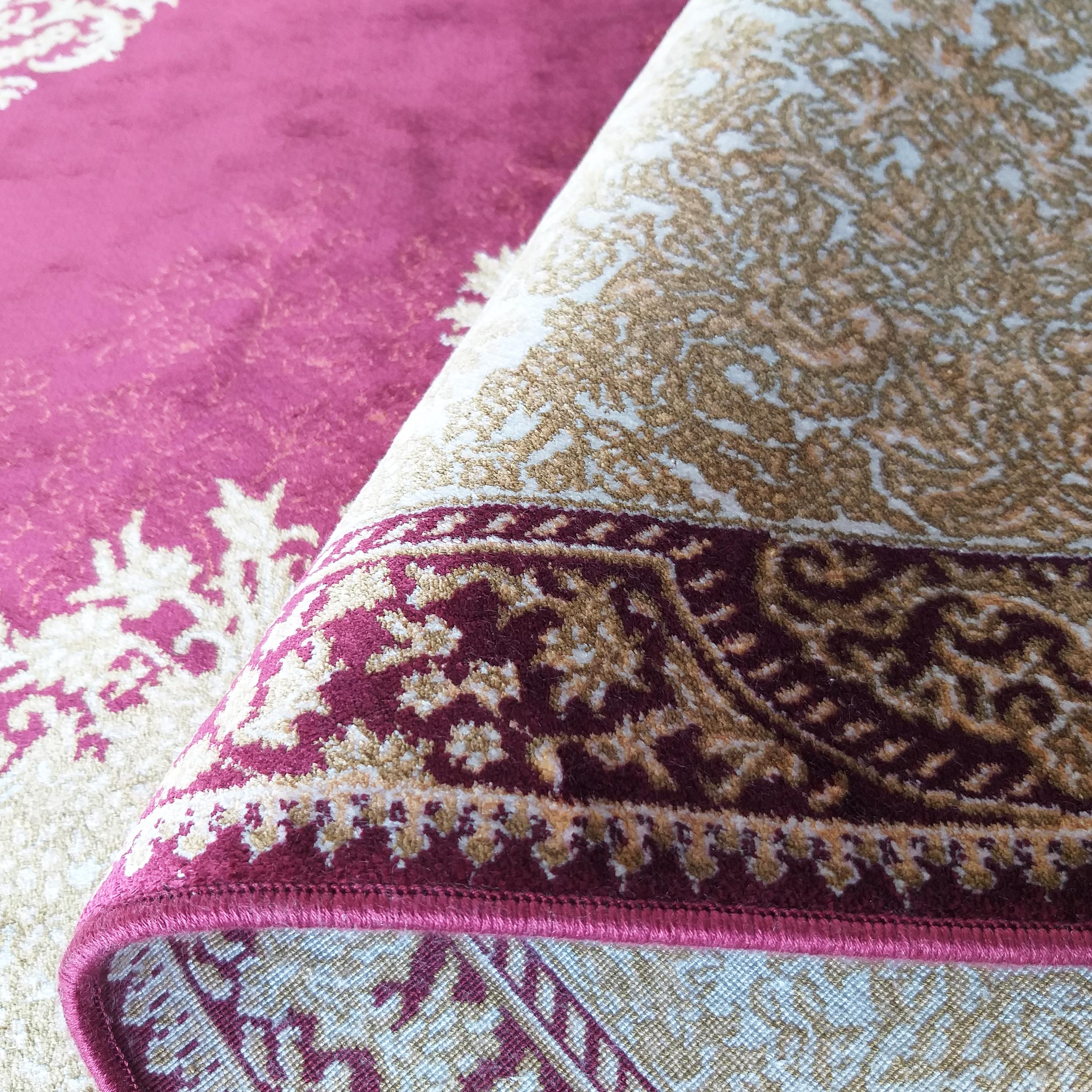 Tapis magenta et beige à motifs floraux détaillés, en partie roulé pour révéler sa surface douce et son tissage arrière