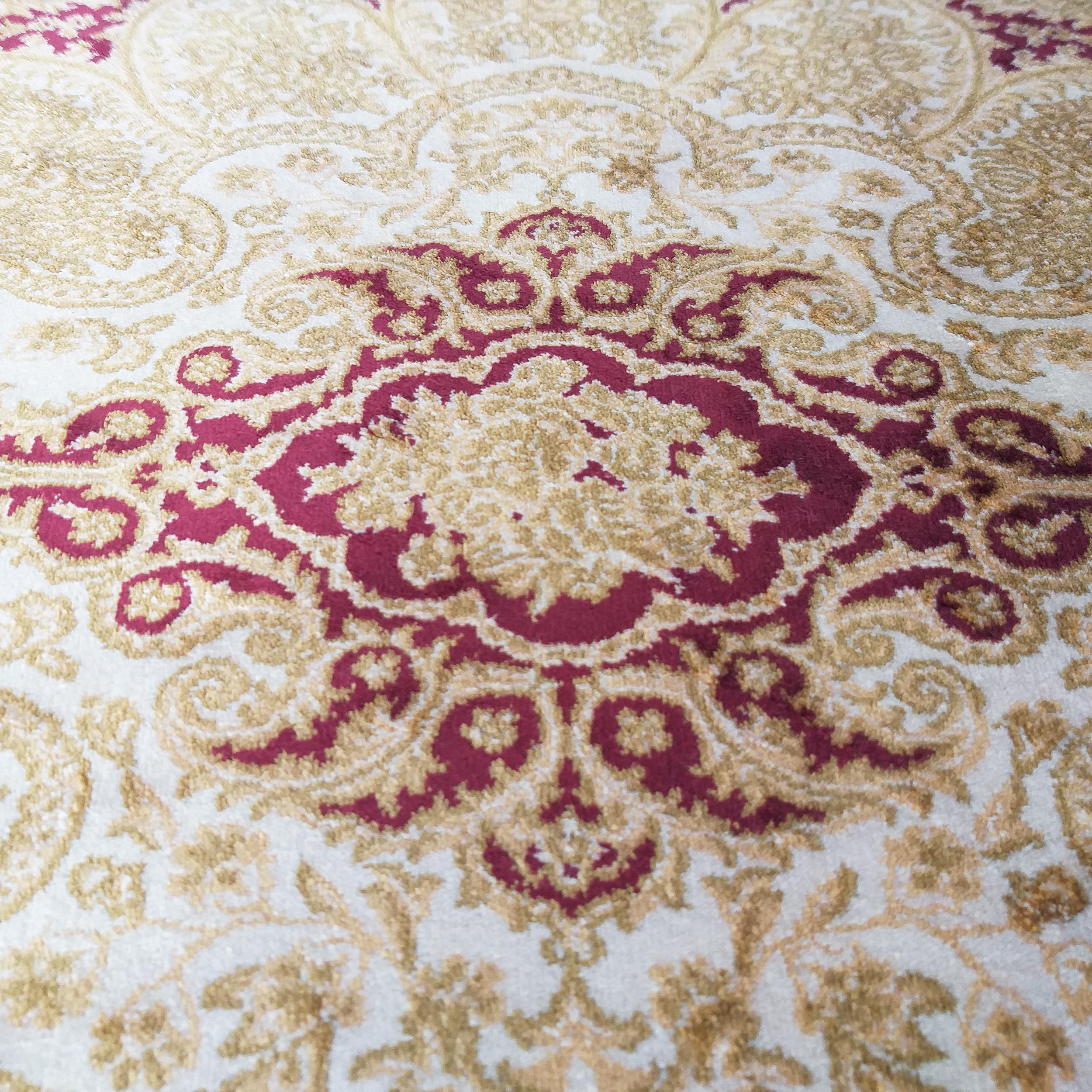 Tapis à motifs ornementaux de style médaillon central bordeaux et arabesques dorées sur fond crème texturé