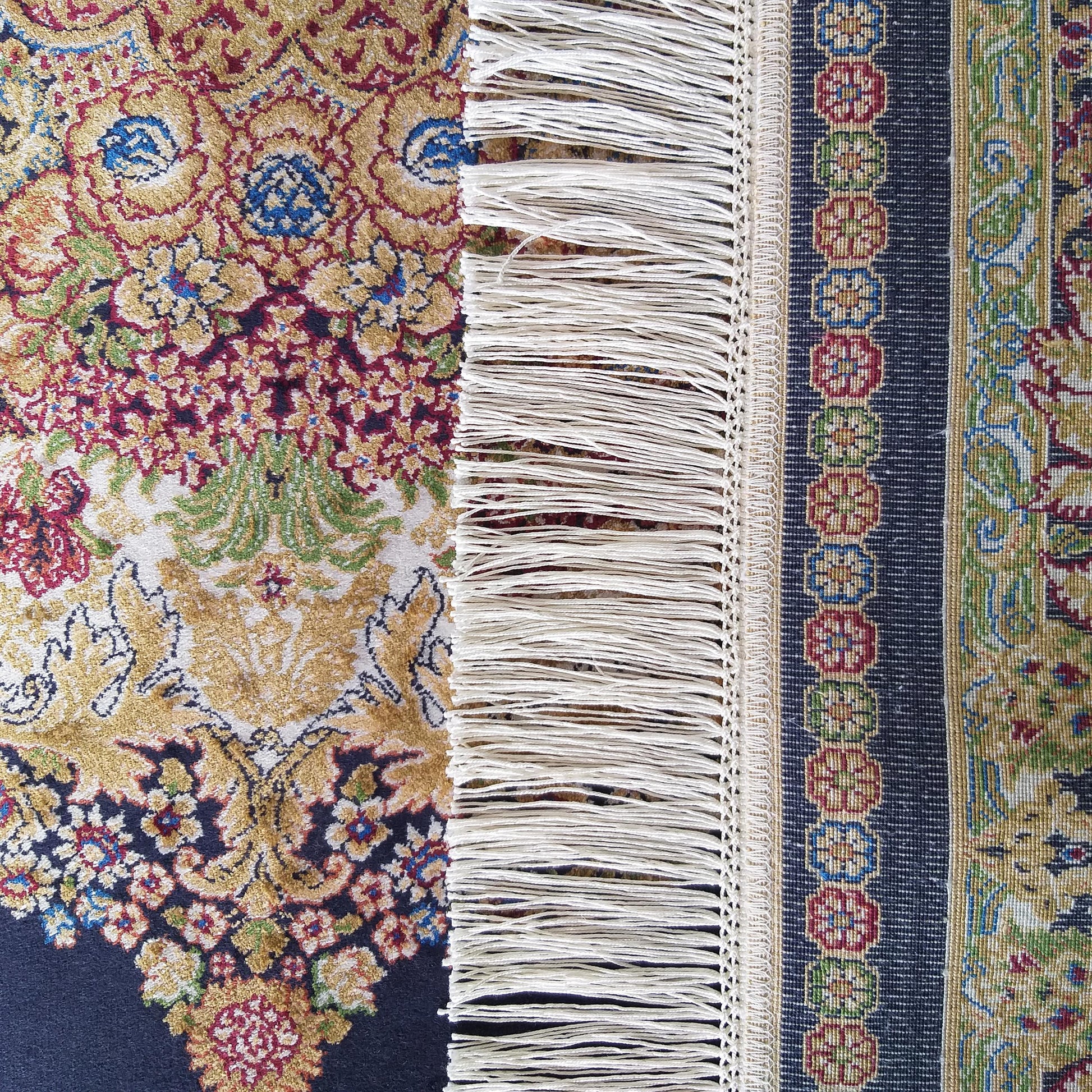Tapis coloré aux motifs floraux or, rouge, bleu et vert, avec des franges blanches et une bordure bleue marine à motifs géométriques