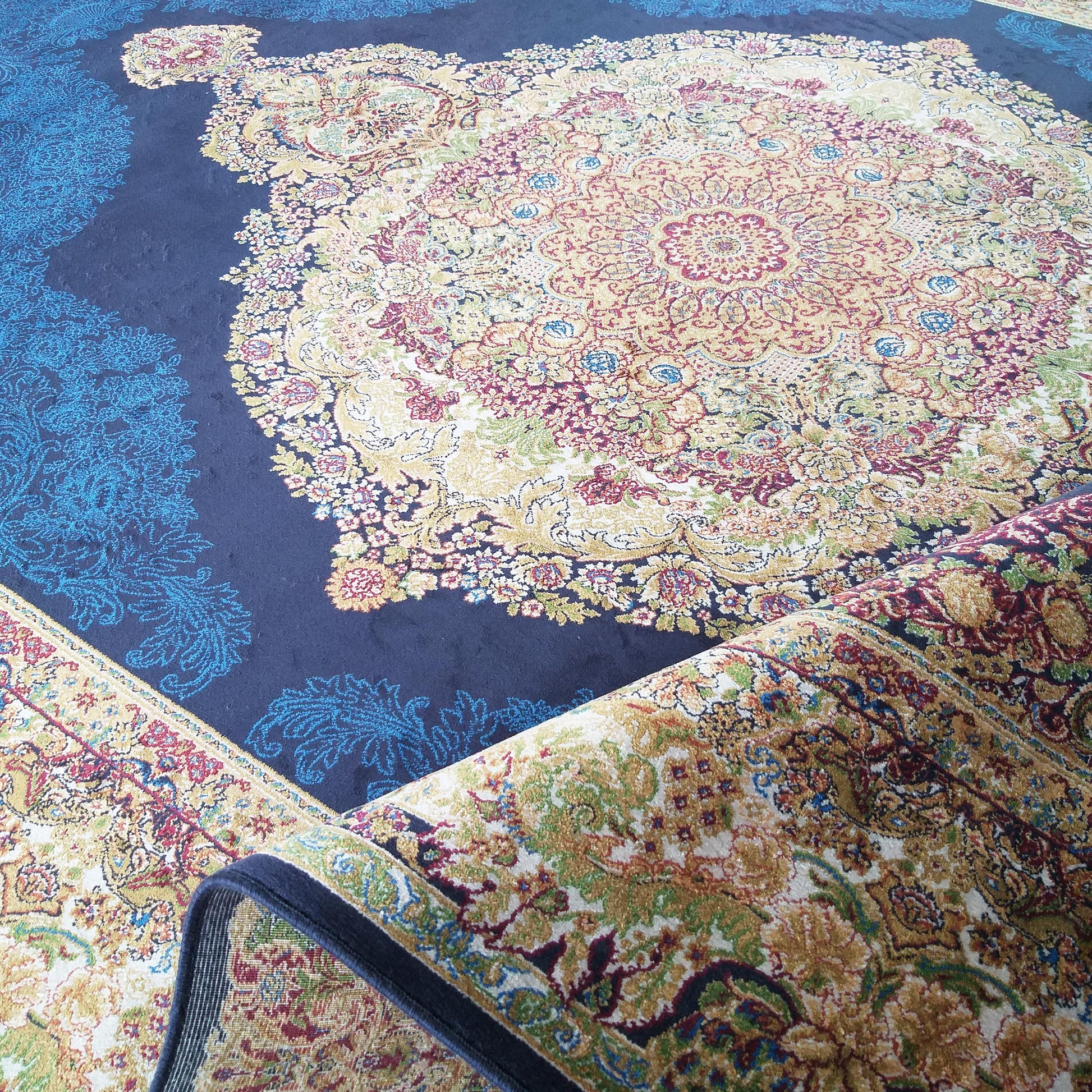 Grand tapis bleu marine à motifs floraux et médaillon central orné de couleurs vives, partiellement enroulé