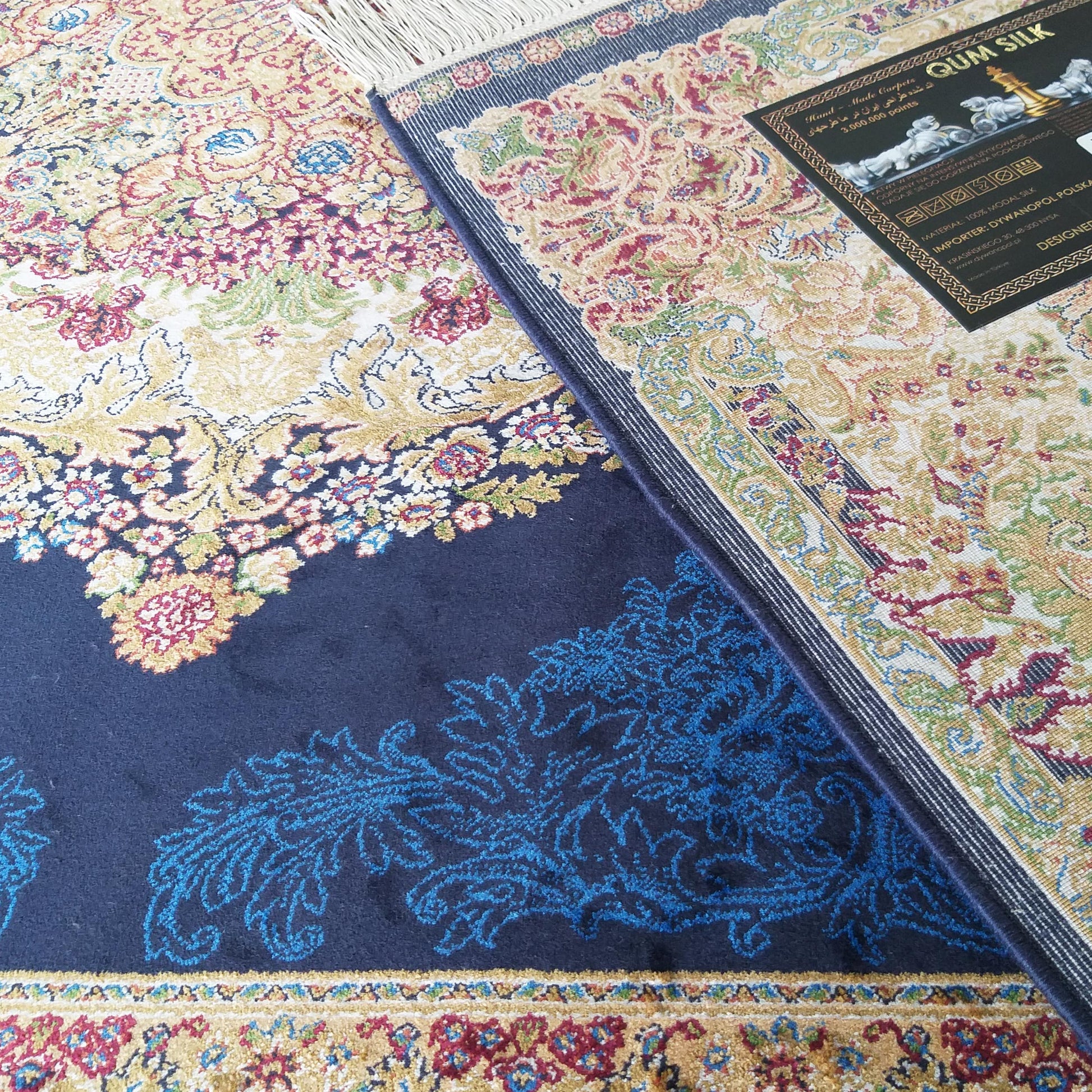 Gros plan d'un tapis aux motifs floraux dorés, rouges et verts, avec des franges et une section bleue nuit à arabesques bleues