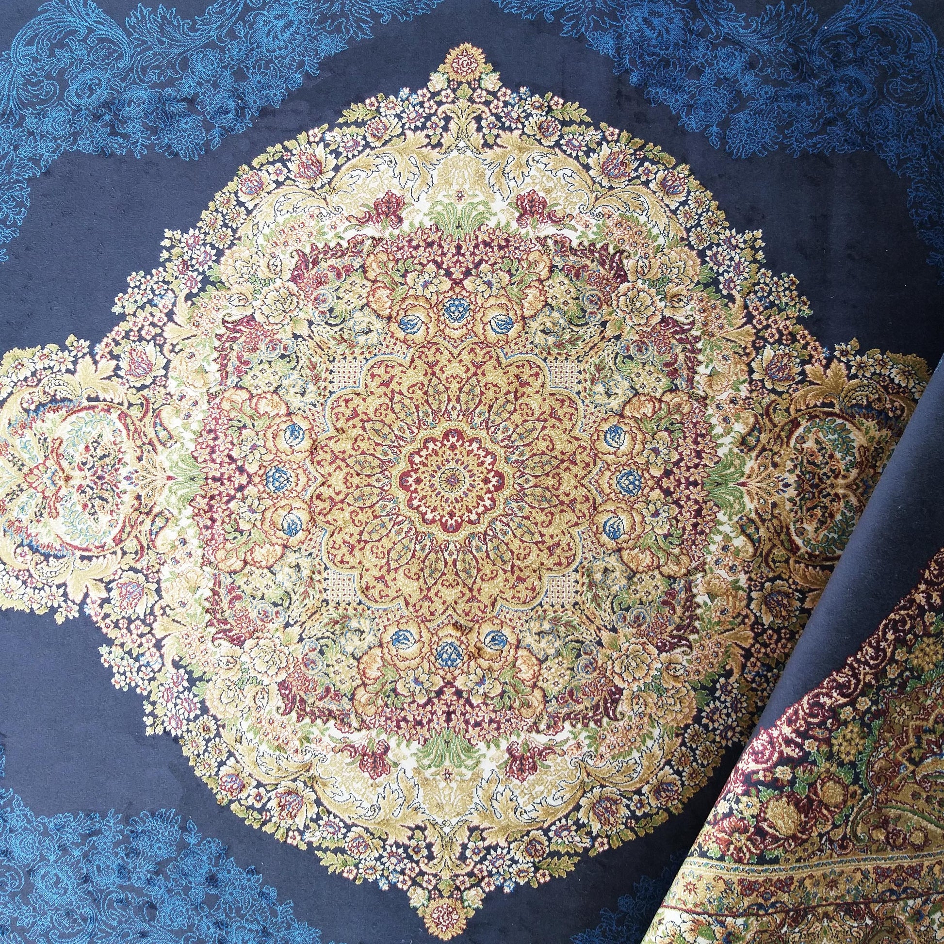 Tapis bleu foncé avec un grand médaillon central aux motifs floraux dorés, rouges et verts, et des motifs bleus sur les bordures