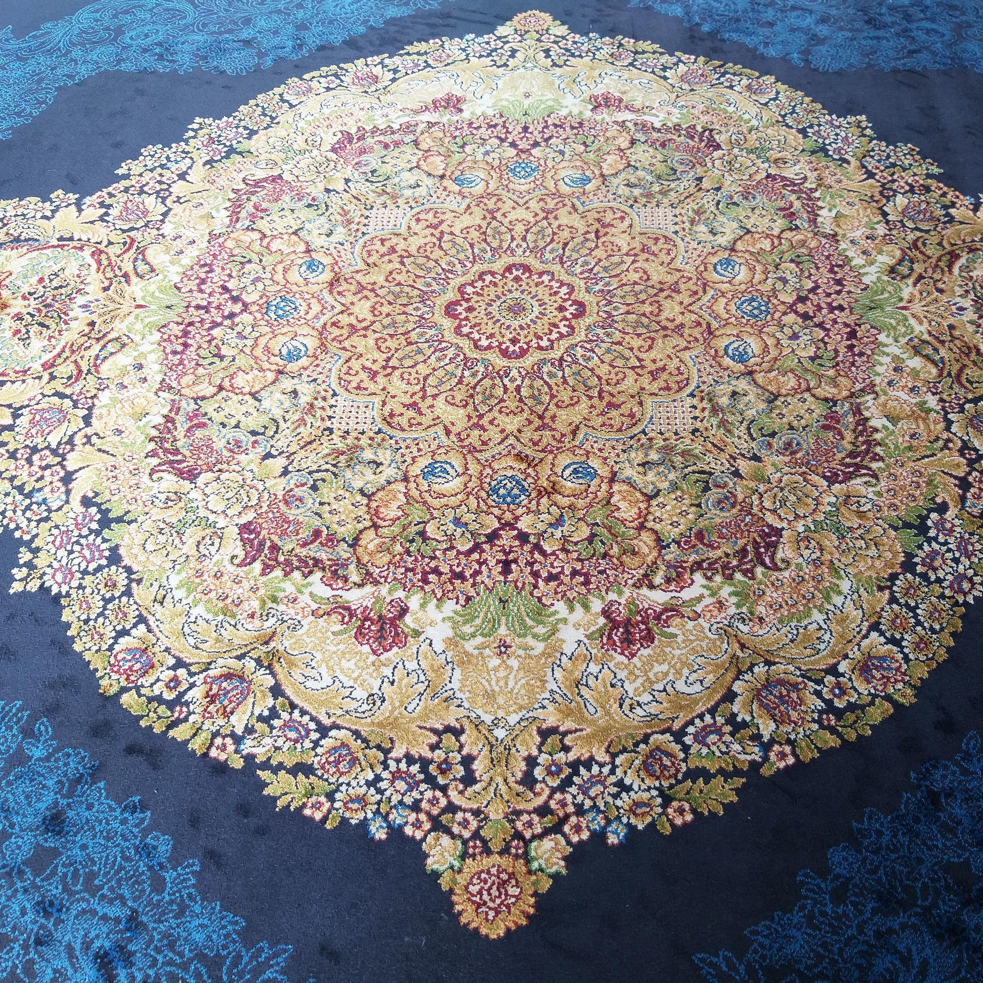 Tapis orné d'un grand médaillon floral central aux teintes dorées, rouges, crème et bleues, sur un fond bleu marine avec des motifs filigranes bleus clairs
