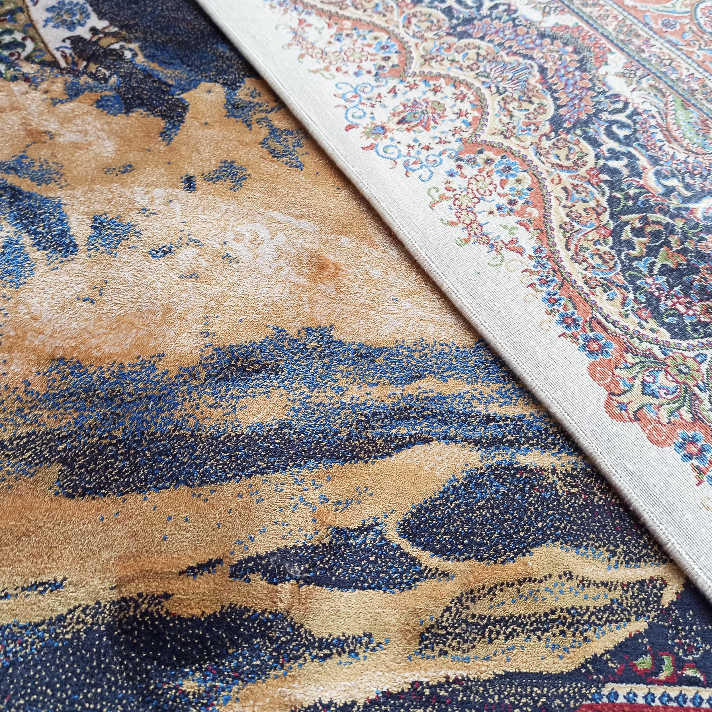 Tapis doré à motifs abstraits bleus sous un tapis persan clair à volutes florales bleues, rouges et vertes