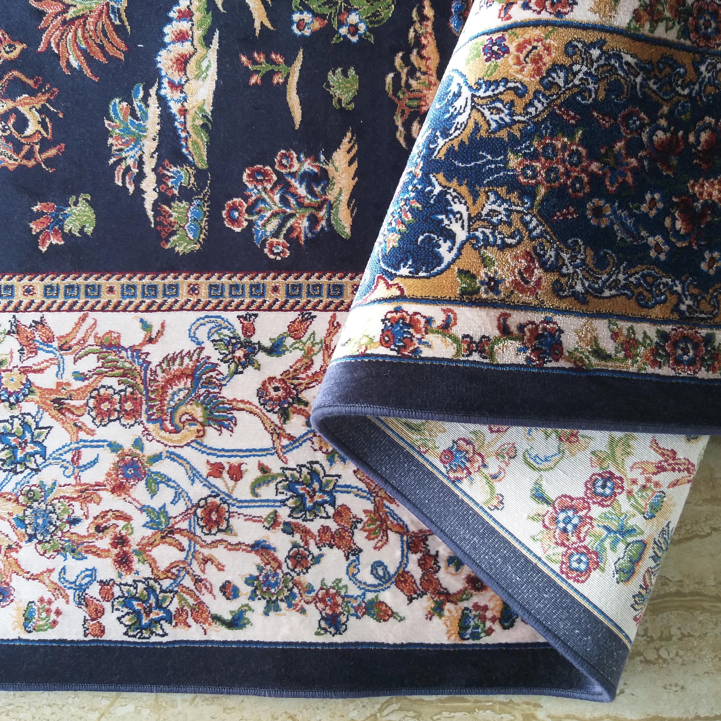 Tapis à poils ras aux motifs floraux et ornementaux élaborés, sur fond bleu marine et crème, partiellement enroulé