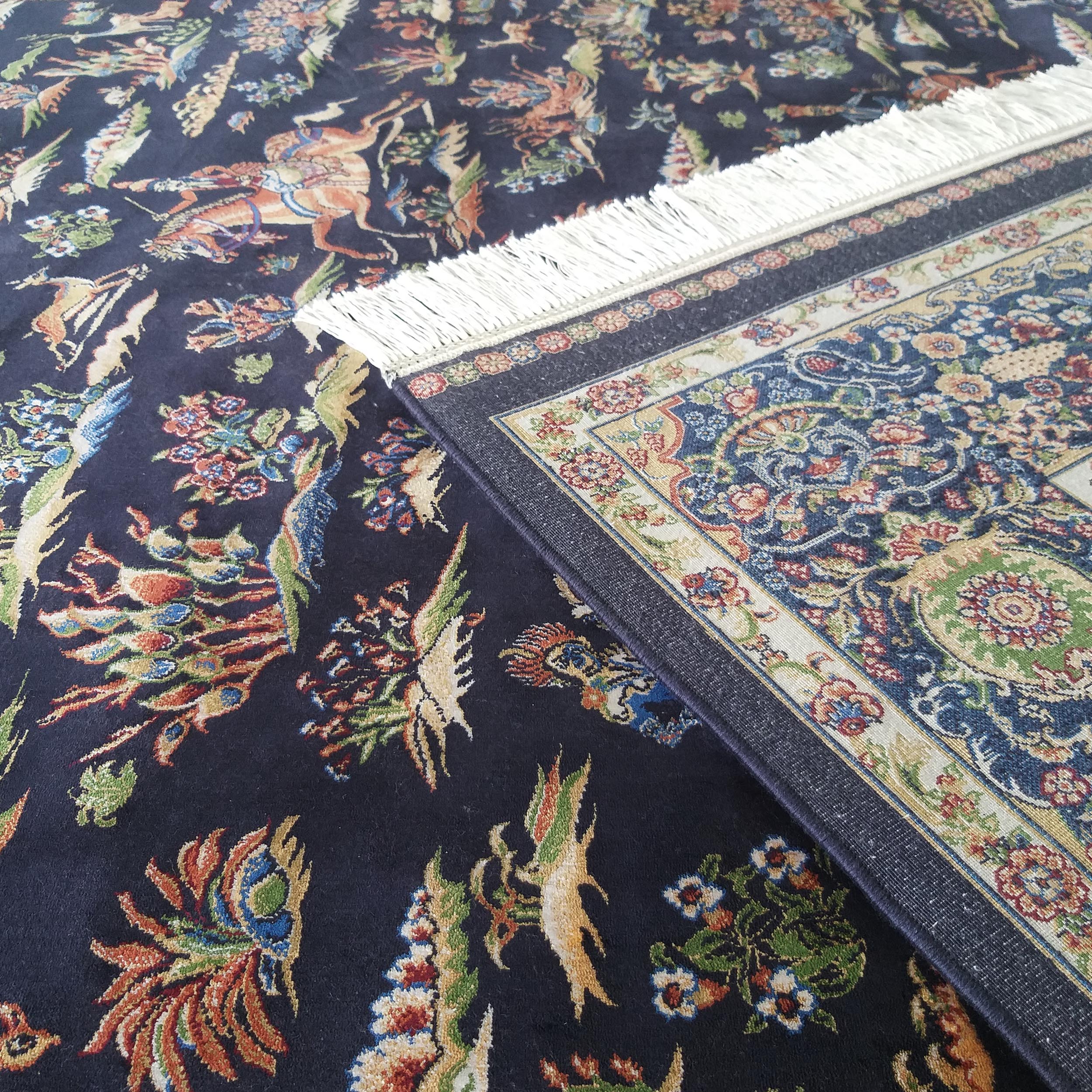 Tapis bleu nuit orné de motifs complexes d'oiseaux et de fleurs colorés, avec un second tapis à franges apparent
