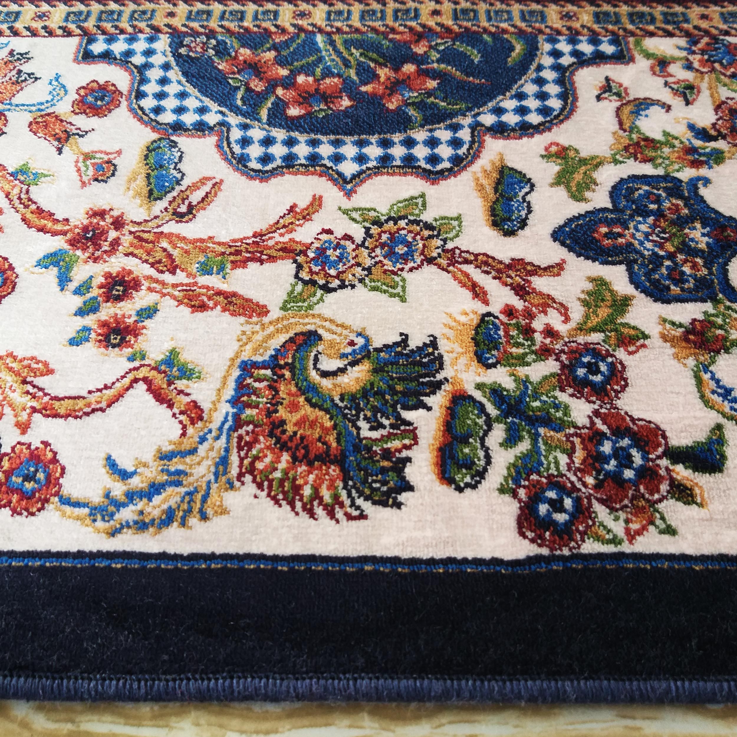 Tapis crème à motifs floraux et d'oiseaux stylisés, aux couleurs vives bleues, rouges, vertes et or, bordé de bleu nuit
