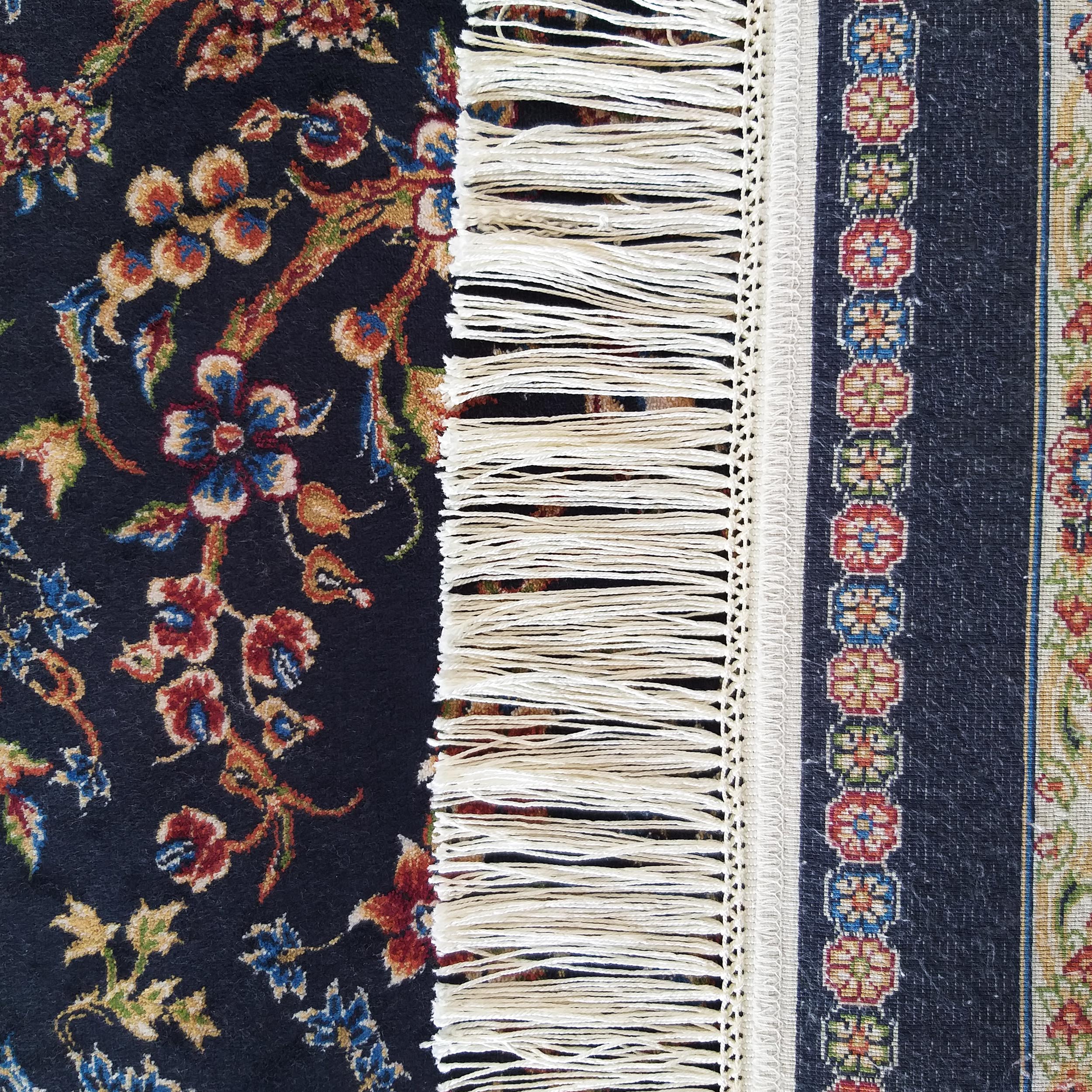 Tapis bleu foncé à motifs floraux rouges, bleus et dorés, avec franges blanches et bordure à motifs géométriques colorés