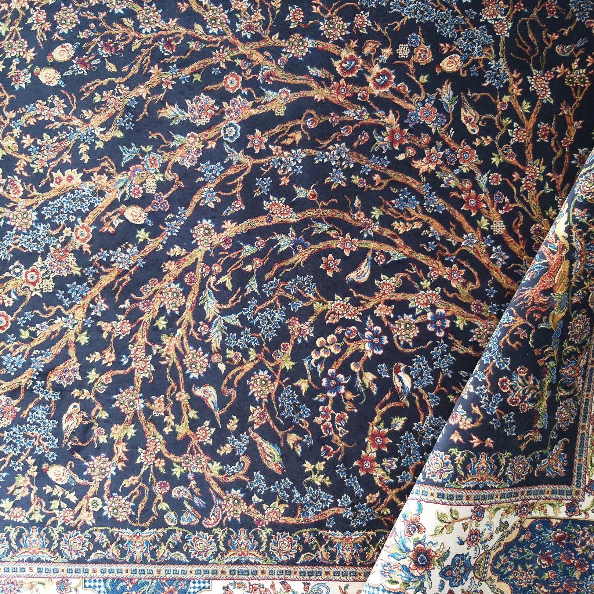 Tapis bleu foncé à motifs floraux détaillés de branches et d'oiseaux multicolores, avec une bordure claire enroulée