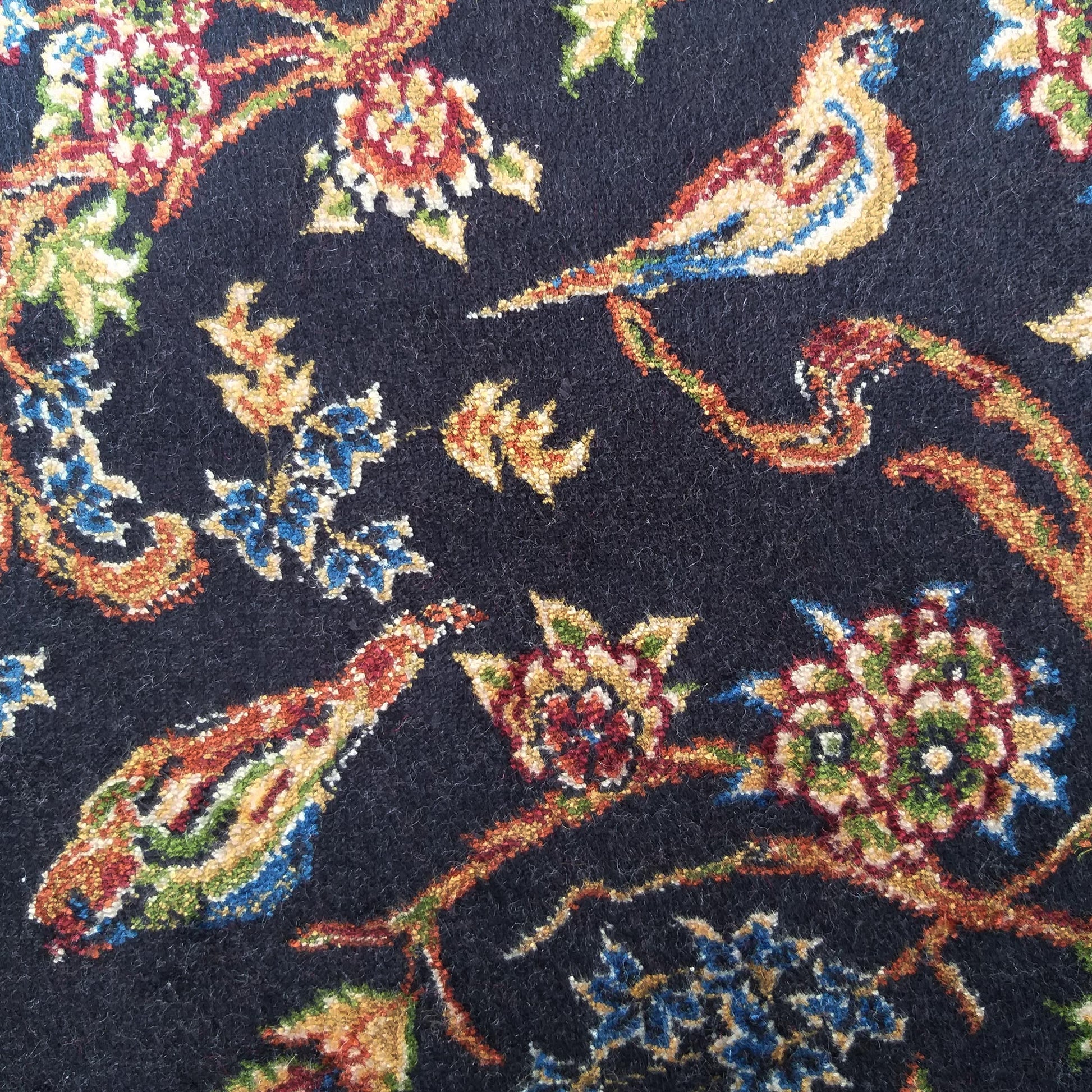 Tapis au fond bleu marine orné de motifs floraux et d'oiseaux. Les couleurs dominantes sont le rouge, le jaune, le bleu et le vert