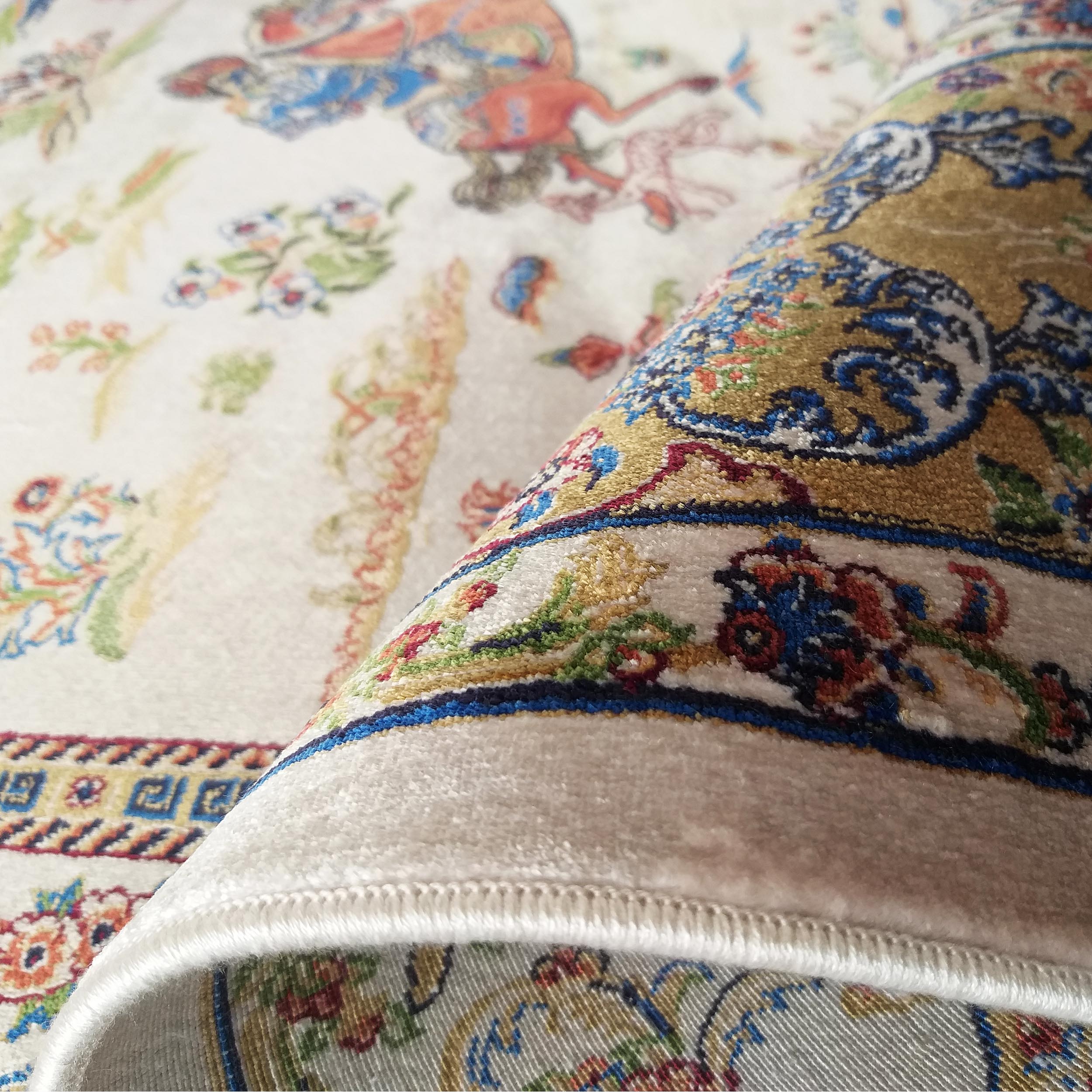 Tapis moelleux crème à motifs floraux et figures colorés, une partie est roulée dévoilant une bordure ornée d'arabesques bleues et dorées