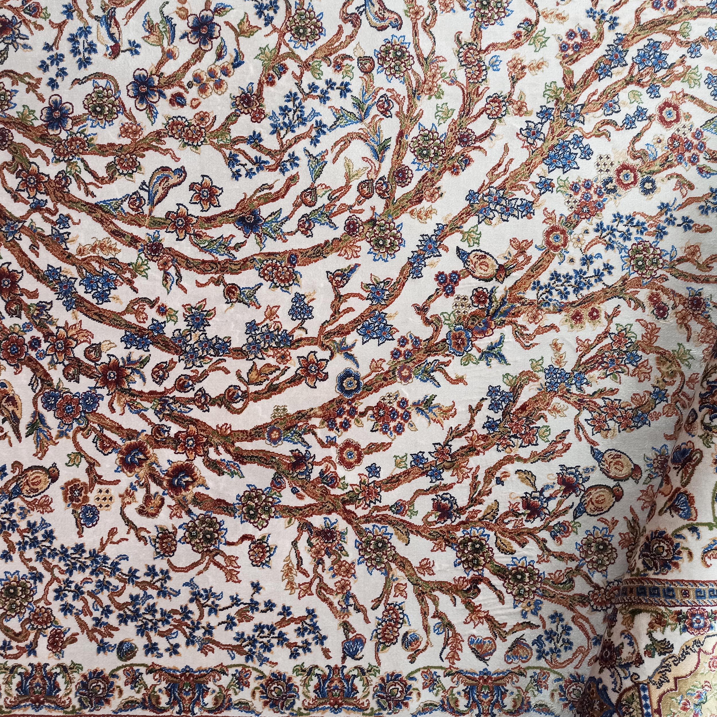 Tapis crème au motif floral détaillé, composé de branches marron, de fleurs bleues, rouges, ocres et de feuilles vertes