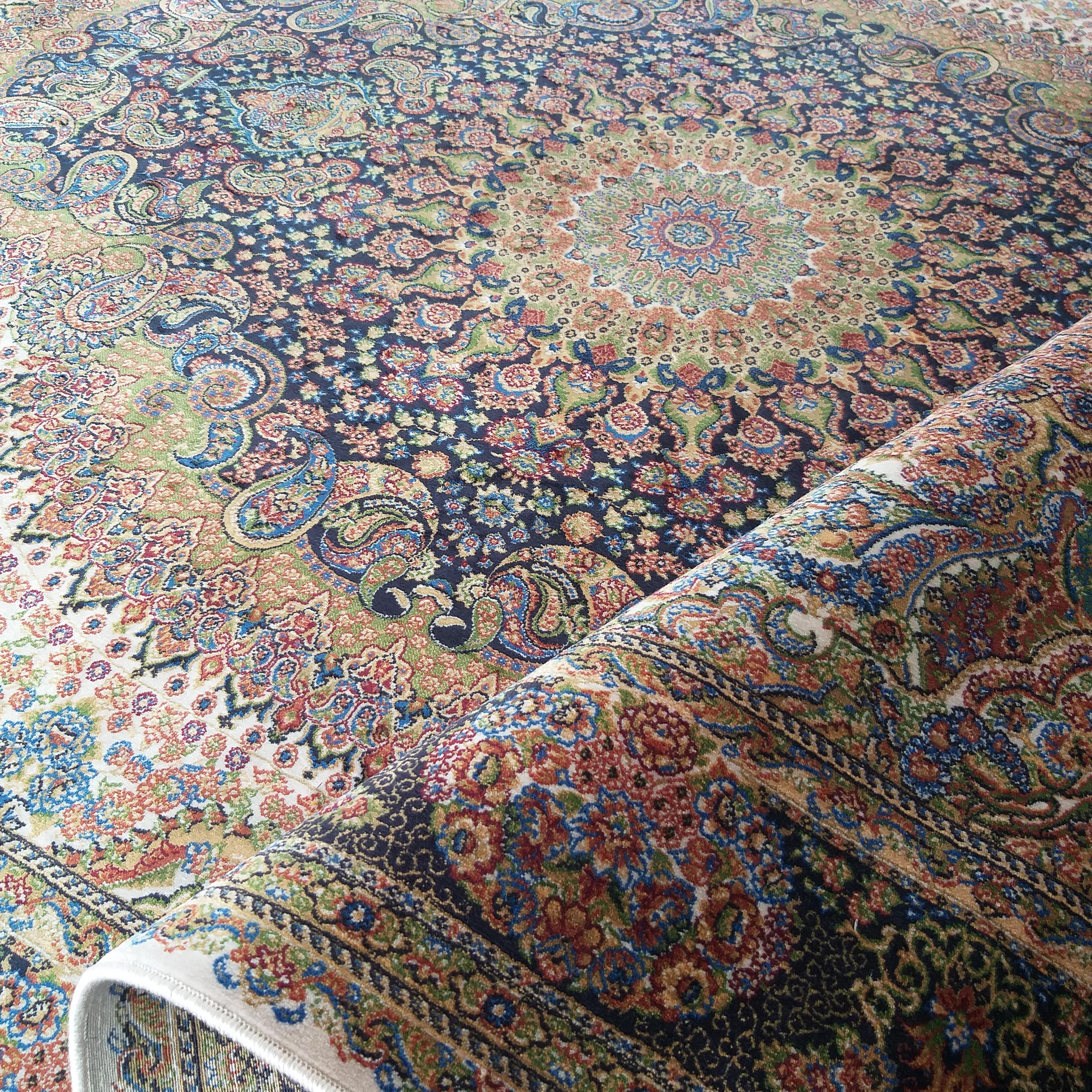 Tapis persan aux motifs floraux et cachemire multicolores (bleu, rouge, vert, or), partiellement enroulé vers l'avant