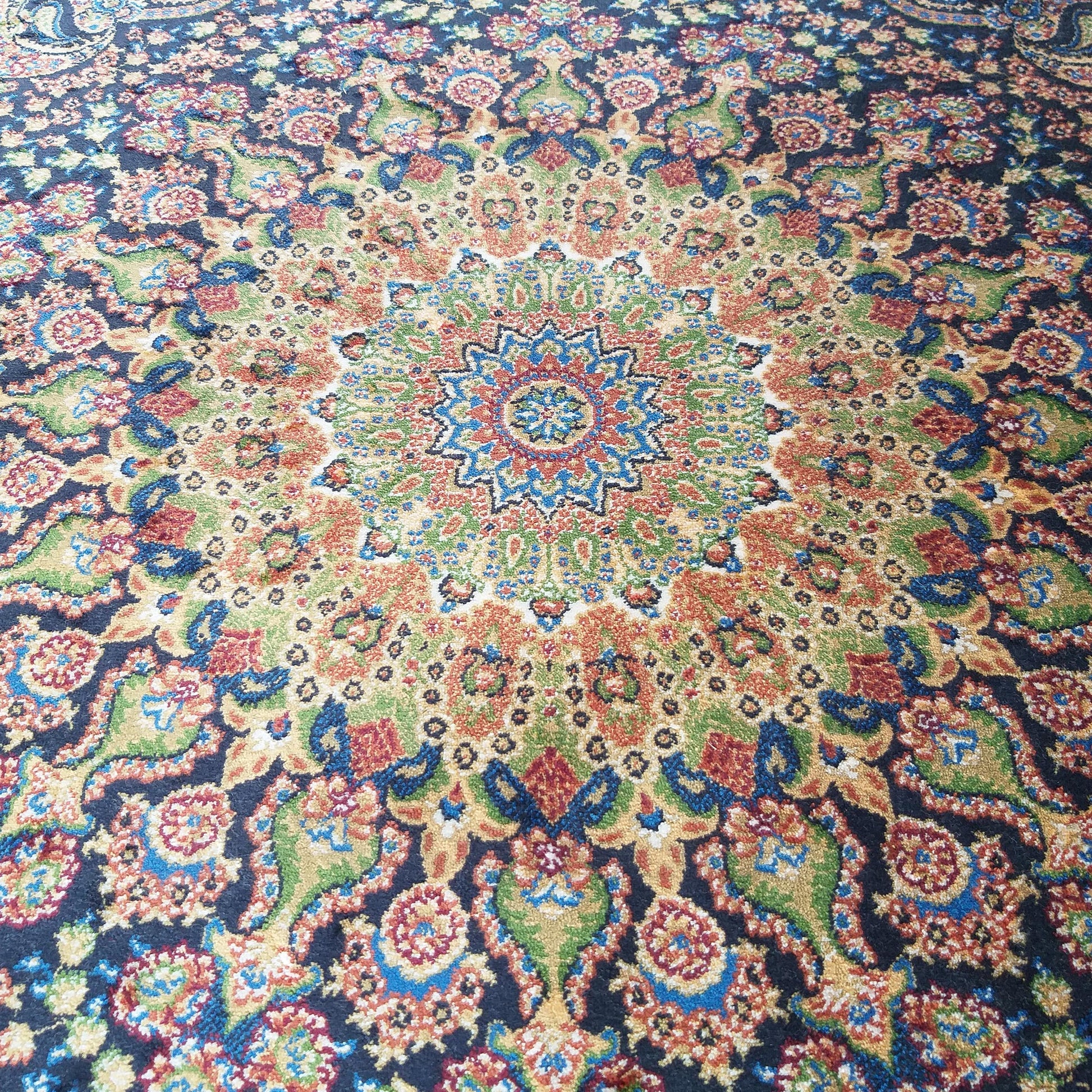 Tapis oriental à motifs floraux et cachemire, avec un médaillon central étoilé aux couleurs vives (bleu, or, rouge, vert) sur fond bleu foncé