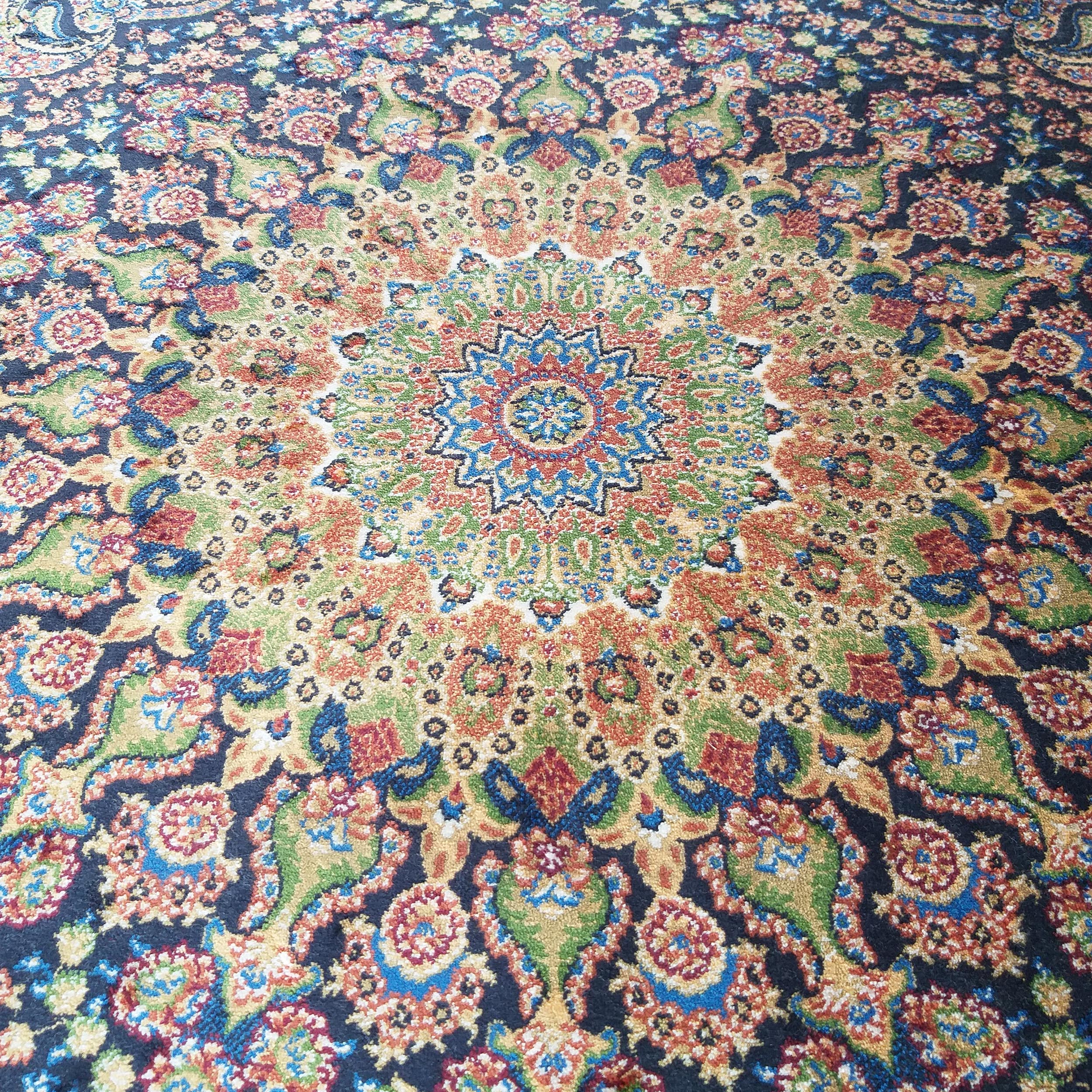 Tapis oriental à motifs floraux et cachemire, avec un médaillon central étoilé aux couleurs vives (bleu, or, rouge, vert) sur fond bleu foncé