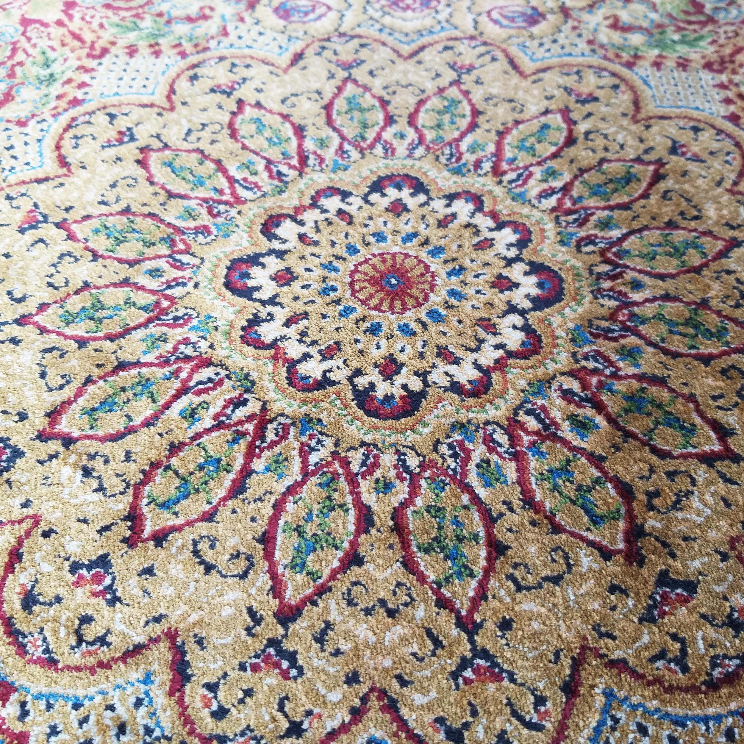 Tapis richement coloré avec un motif central floral et des arabesques en doré, rouge bordeaux, bleu et vert