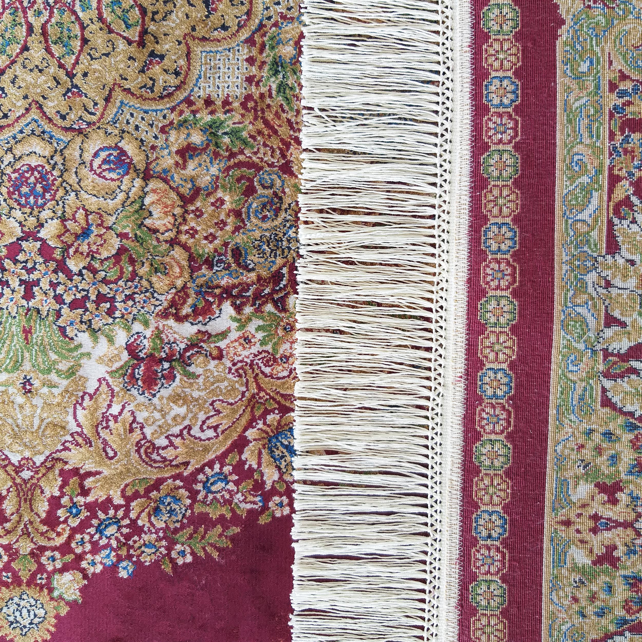 Tapis aux motifs floraux rouges et dorés, séparé par une frange crème d'une bande ornementale à rosettes