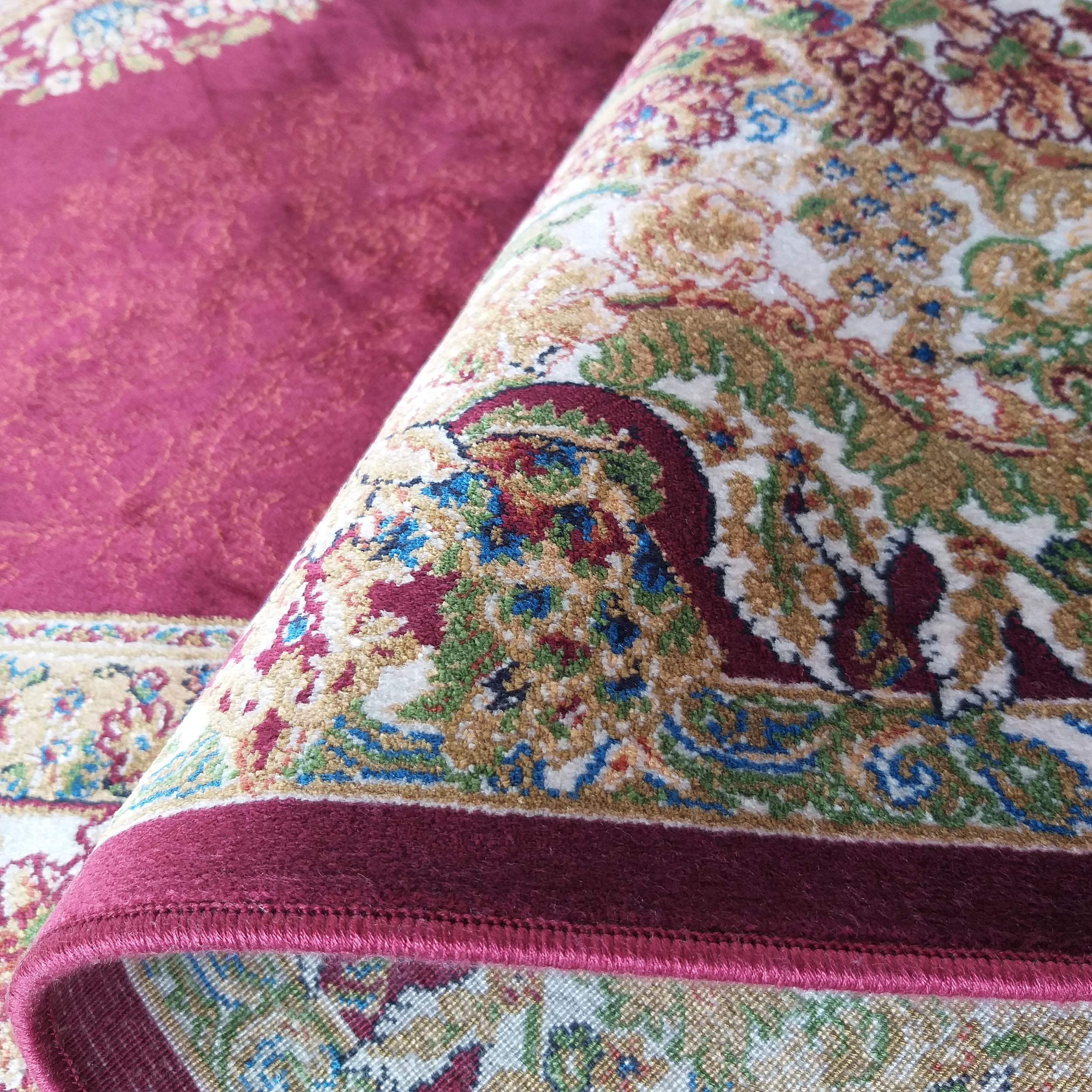 Gros plan sur un tapis au poil court bordeaux, roulé pour dévoiler des motifs floraux beiges, dorés, verts et bleus