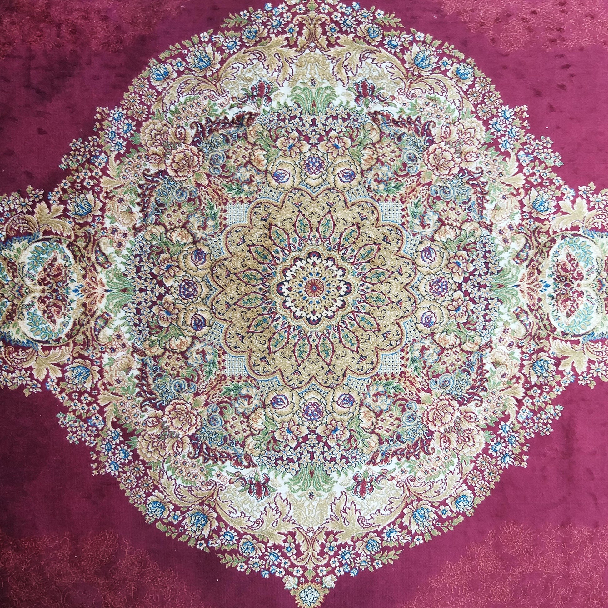 Tapis bordeaux au centre orné d'un grand médaillon floral et ornemental aux teintes dorées, bleues, vertes et crème
