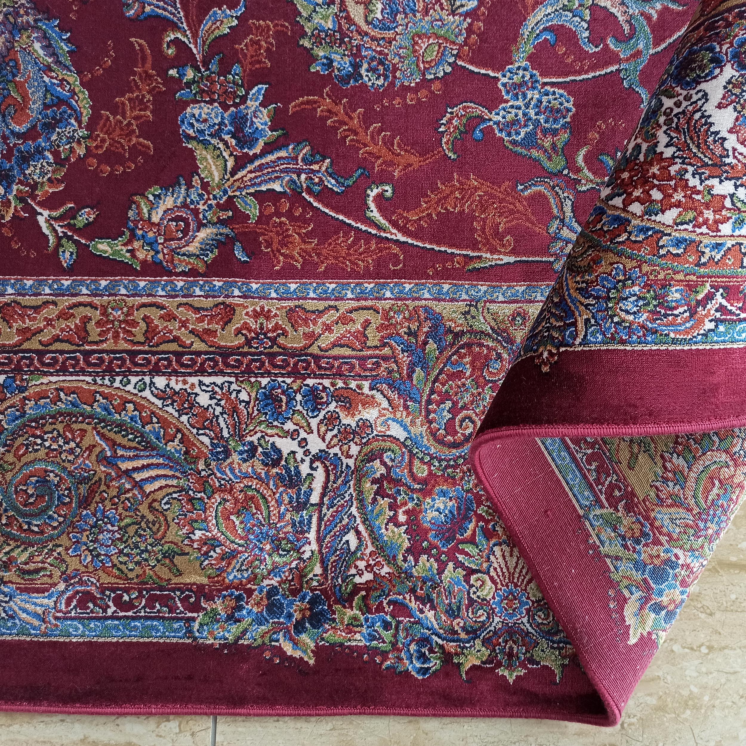 Tapis bordeaux à motifs floraux et cachemire multicolores, partiellement roulé, montrant des bordures détaillées et une texture dense
