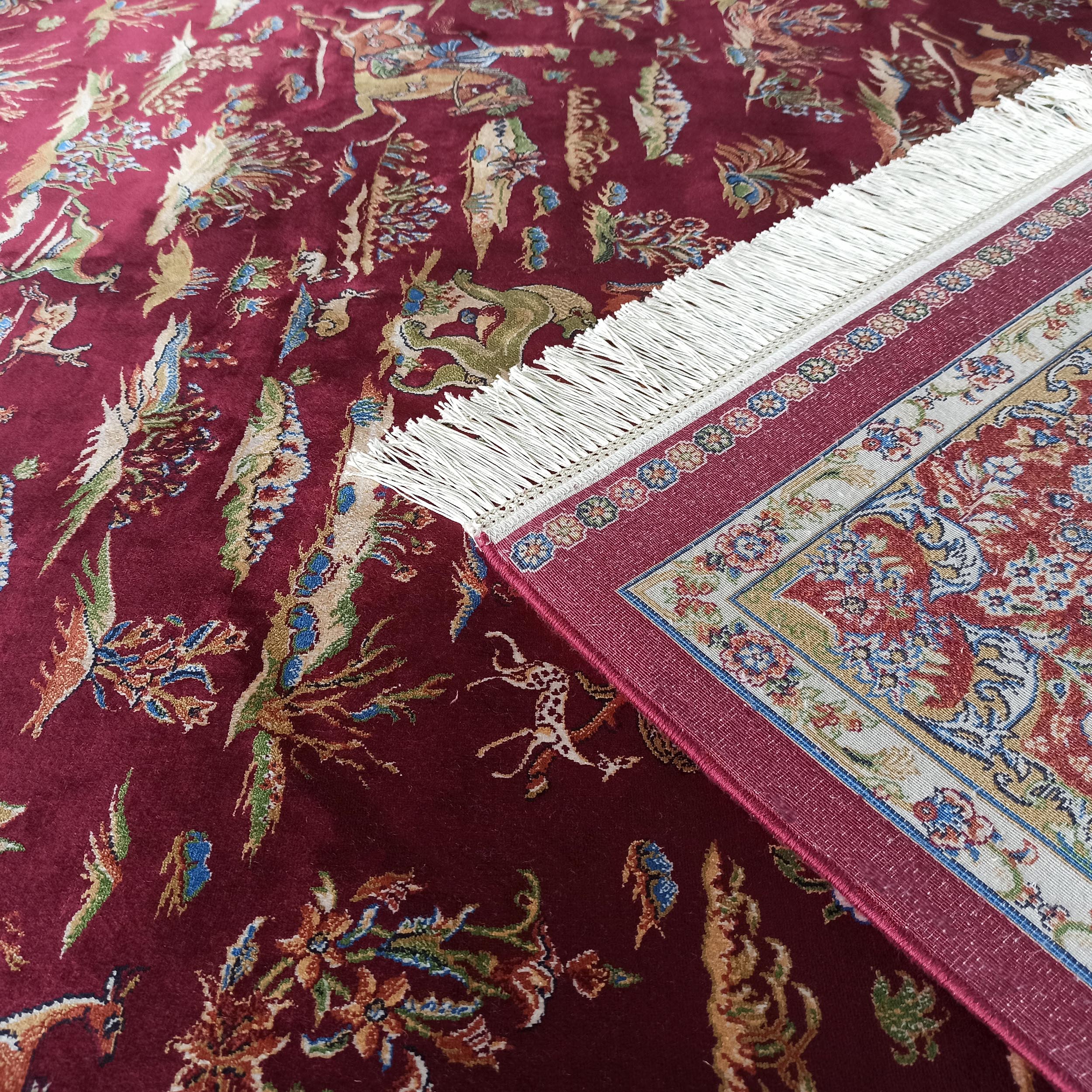 Tapis bordeaux orné de motifs complexes d'animaux et de fleurs, avec des franges blanches sur le côté