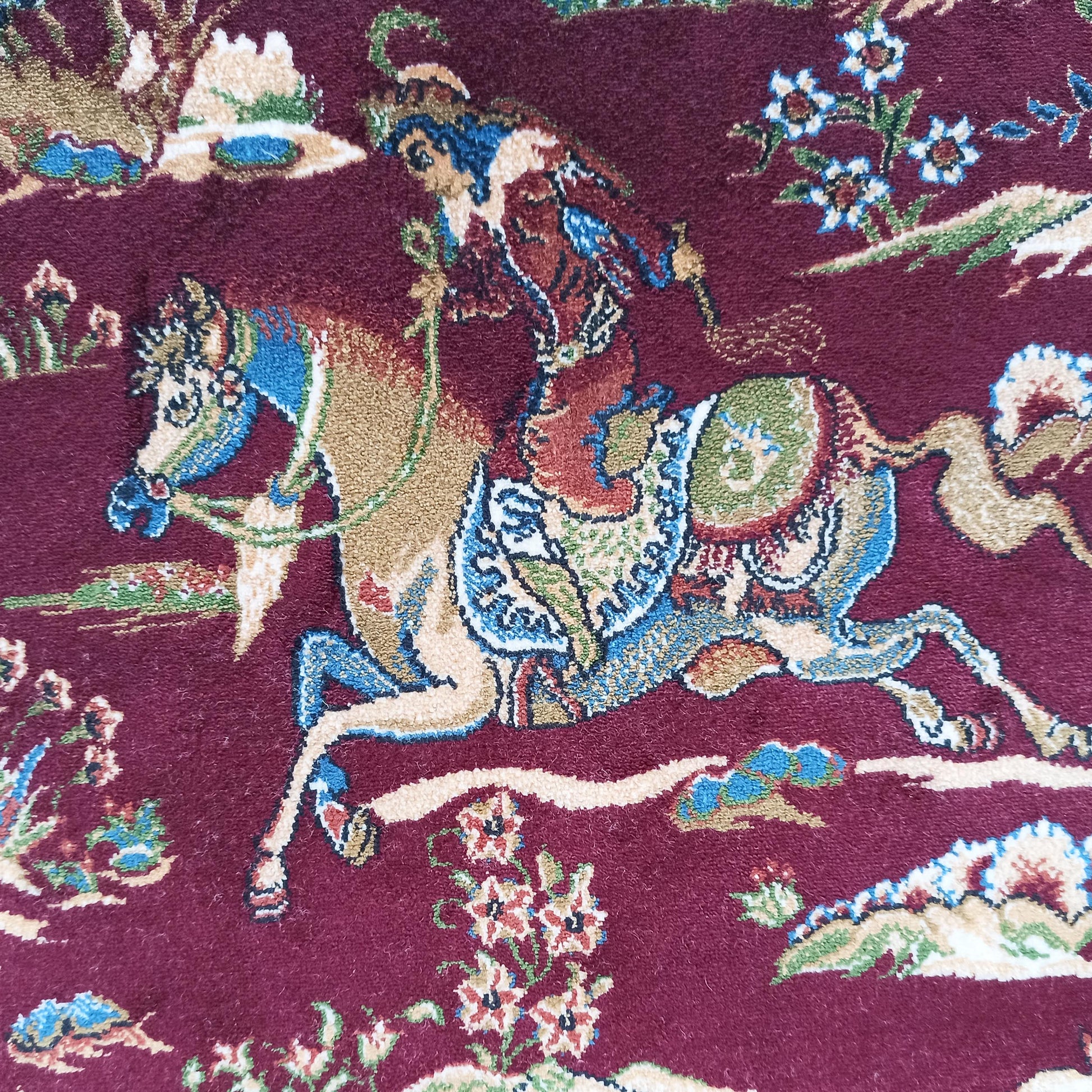 Tapis bordeaux à motifs traditionnels représentant un cavalier sur son cheval avec des fleurs et des paysages