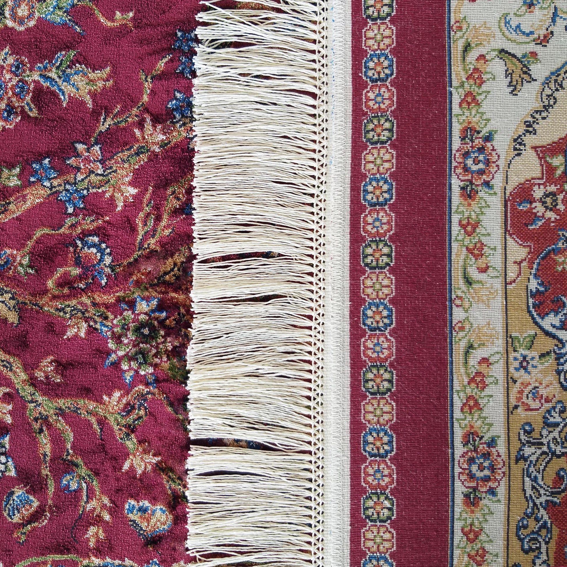 Tapis rouge foncé à motifs floraux. Des franges blanches séparent cette section d'une bordure claire aux motifs variés et colorés