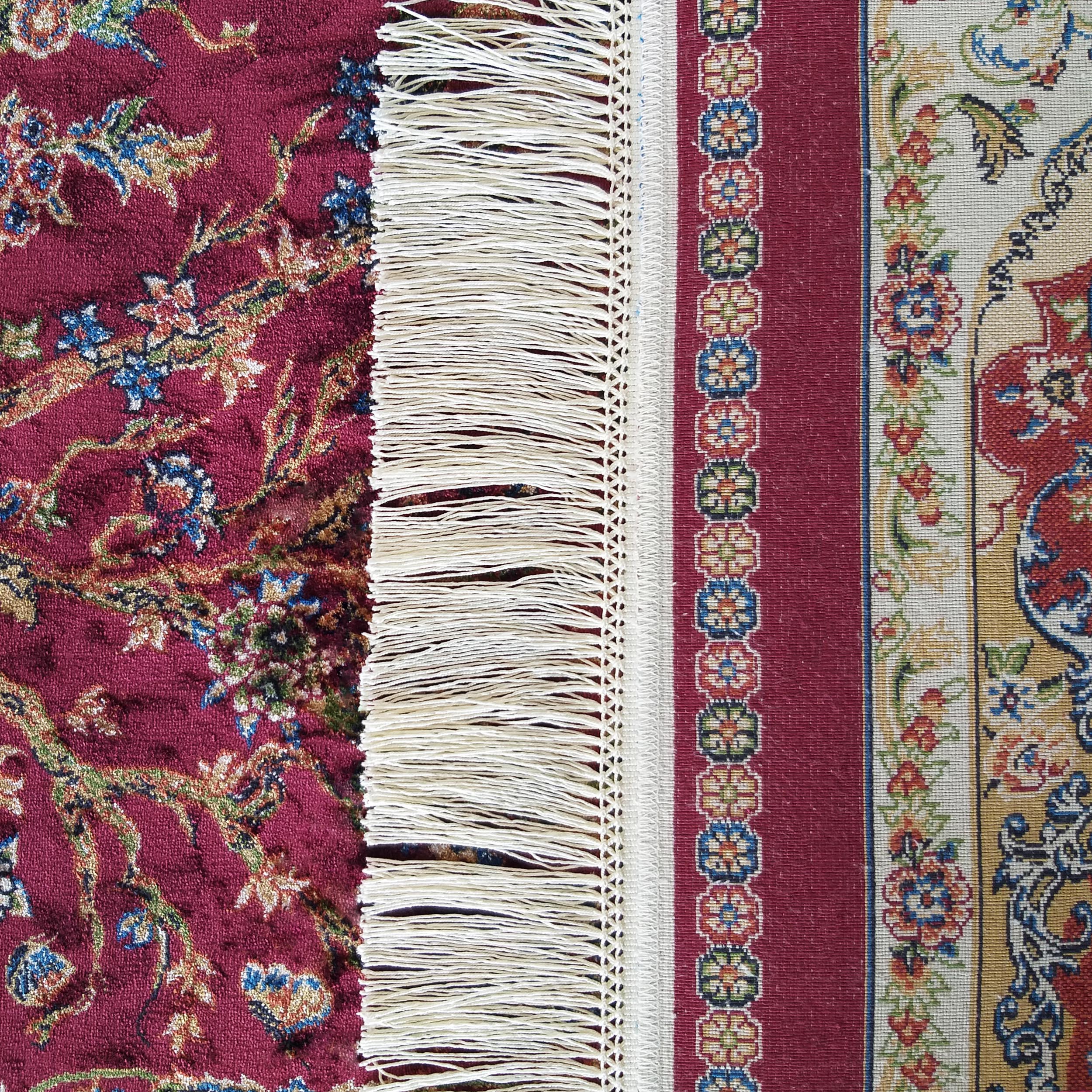 Tapis rouge foncé à motifs floraux. Des franges blanches séparent cette section d'une bordure claire aux motifs variés et colorés