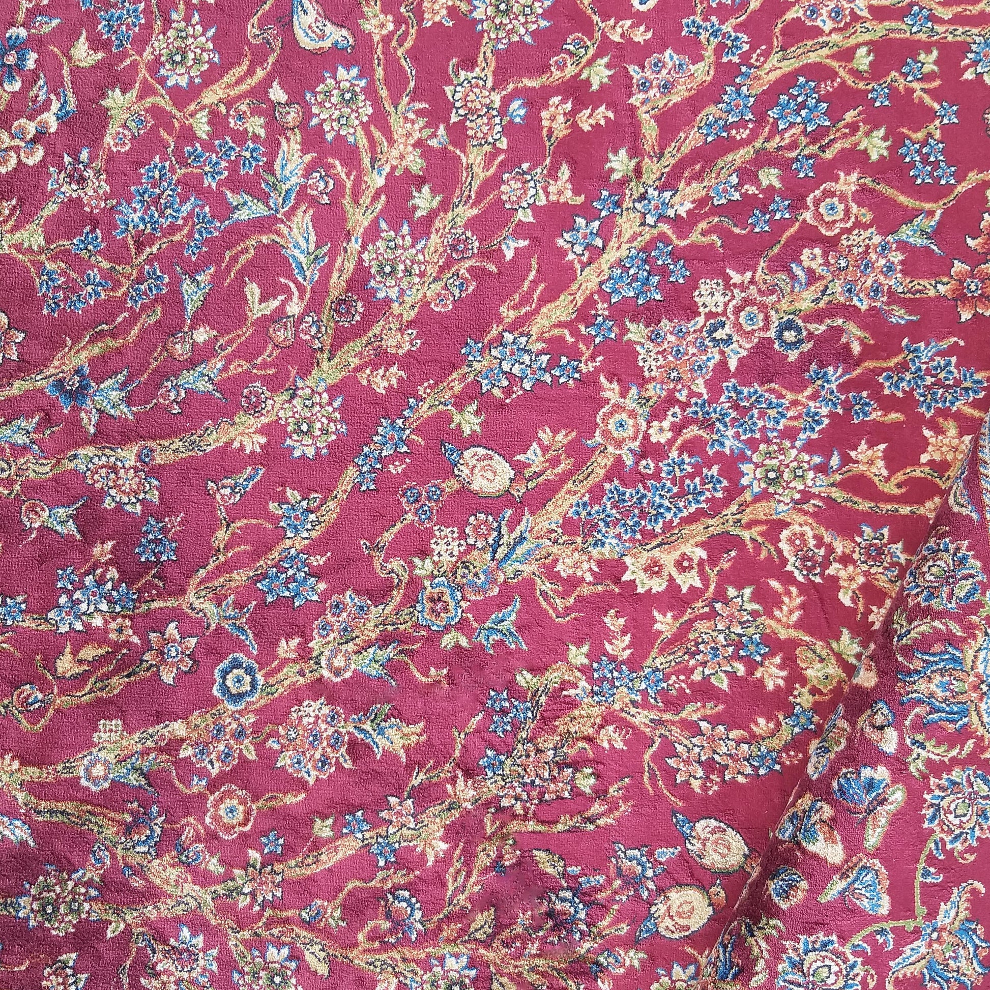 Tapis rouge bordeaux avec un riche motif floral composé de fleurs bleues, crème, vertes et de rinceaux dorés
