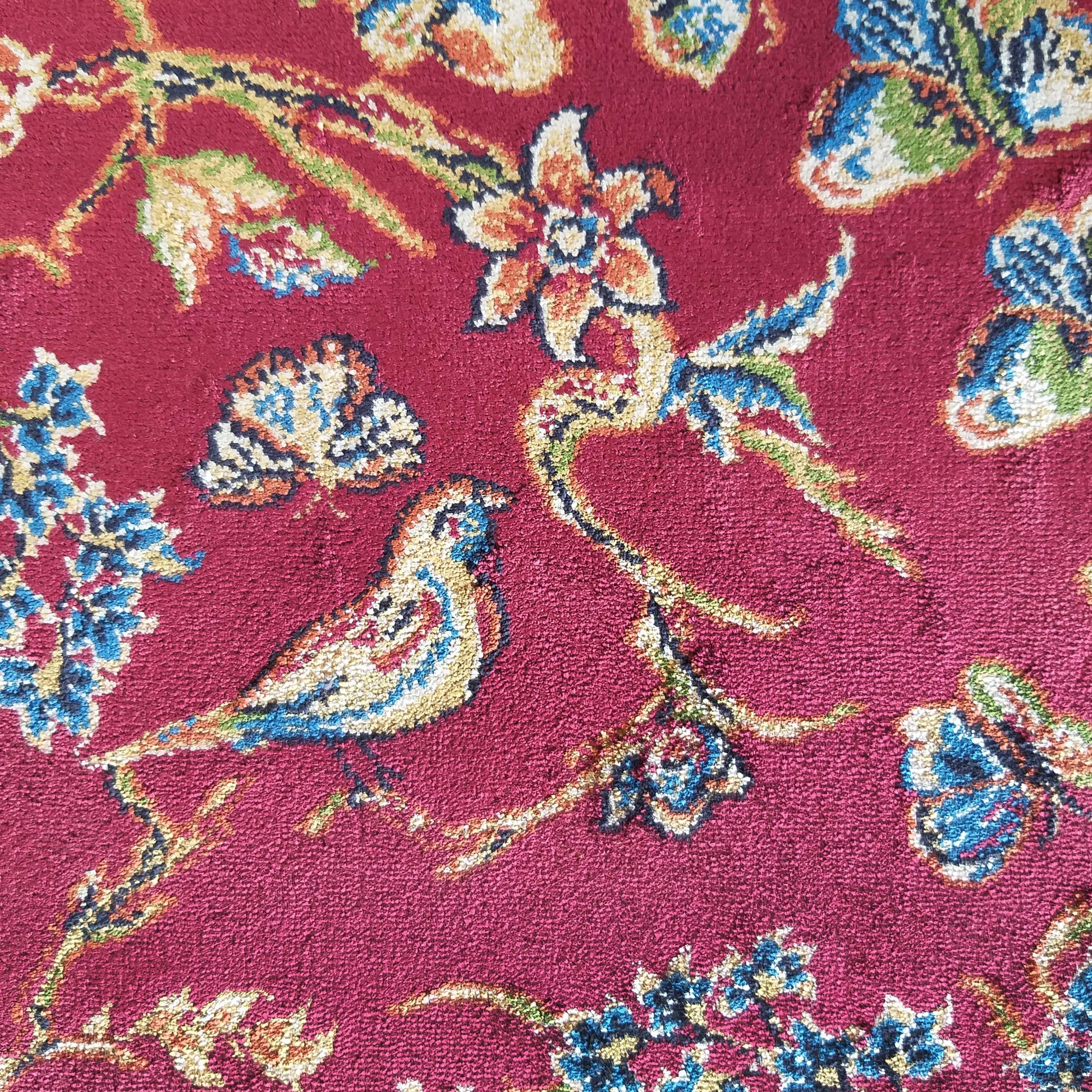 Tapis rouge cramoisi orné de motifs floraux, d'oiseaux et de papillons aux couleurs bleu, jaune, vert et orange