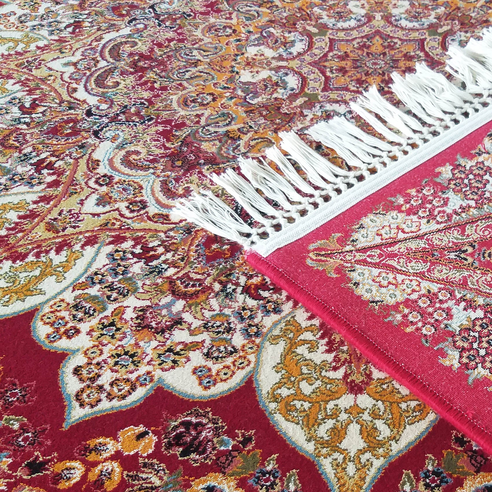 Tapis rouge et crème à motifs floraux et cachemire complexes, avec franges blanches, un coin du tapis replié