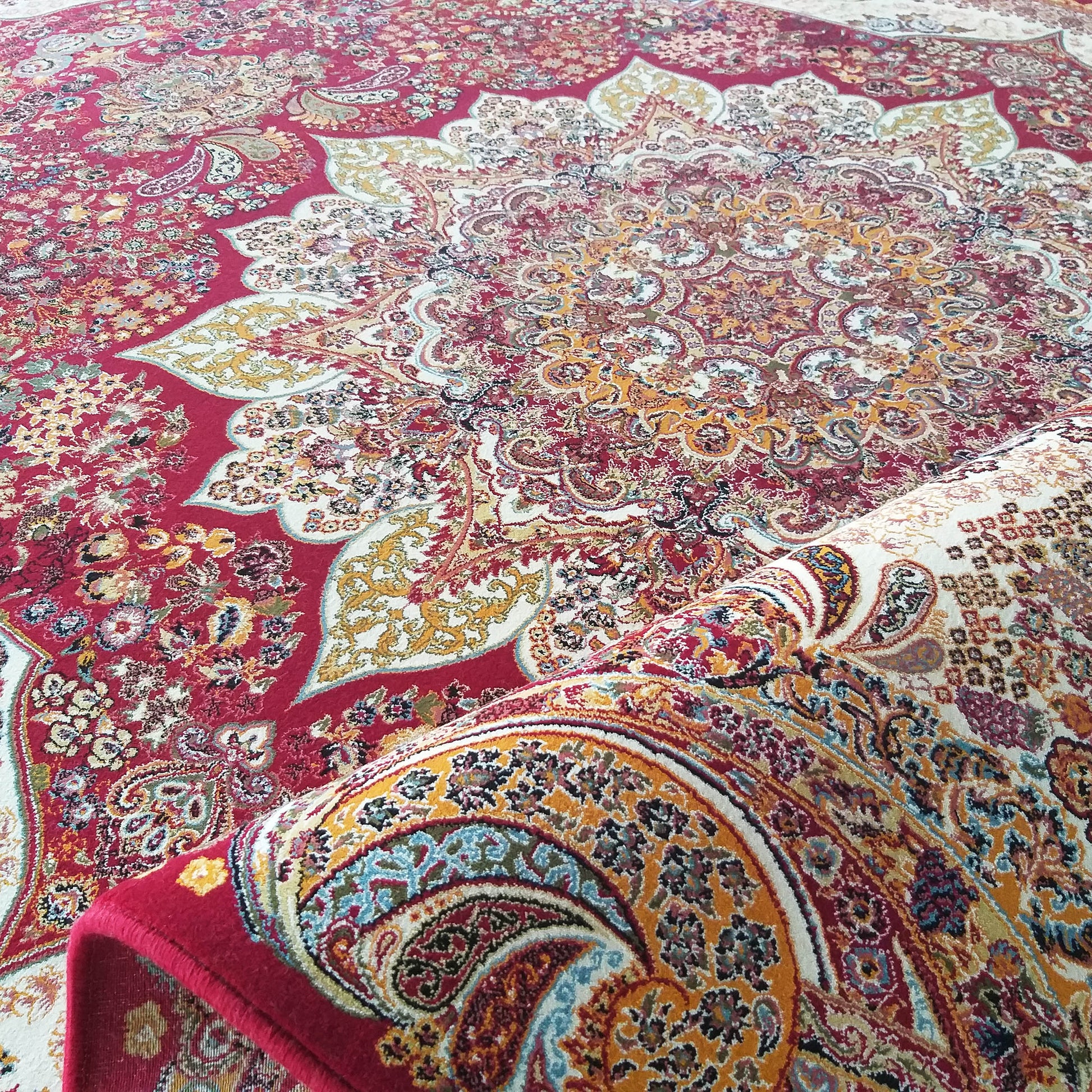 Grand tapis rouge à motifs orientaux détaillés, floraux et médaillons, dans des tons de crème, or et bleu, partiellement roulé