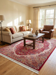 Tapis persan rouge bordeaux à motifs floraux et paisley crème, or et bleu, avec franges, posé sur un parquet clair dans un salon