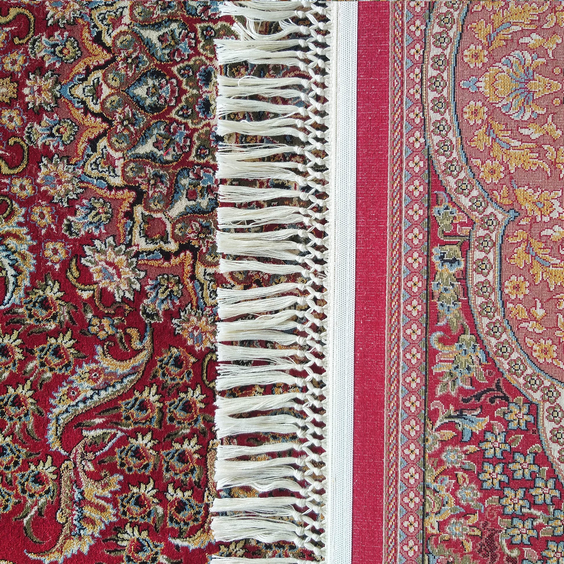 Gros plan d'un tapis rouge et multicolore orné de motifs floraux et cachemire, avec franges crème et une section tissée à motifs géométriques