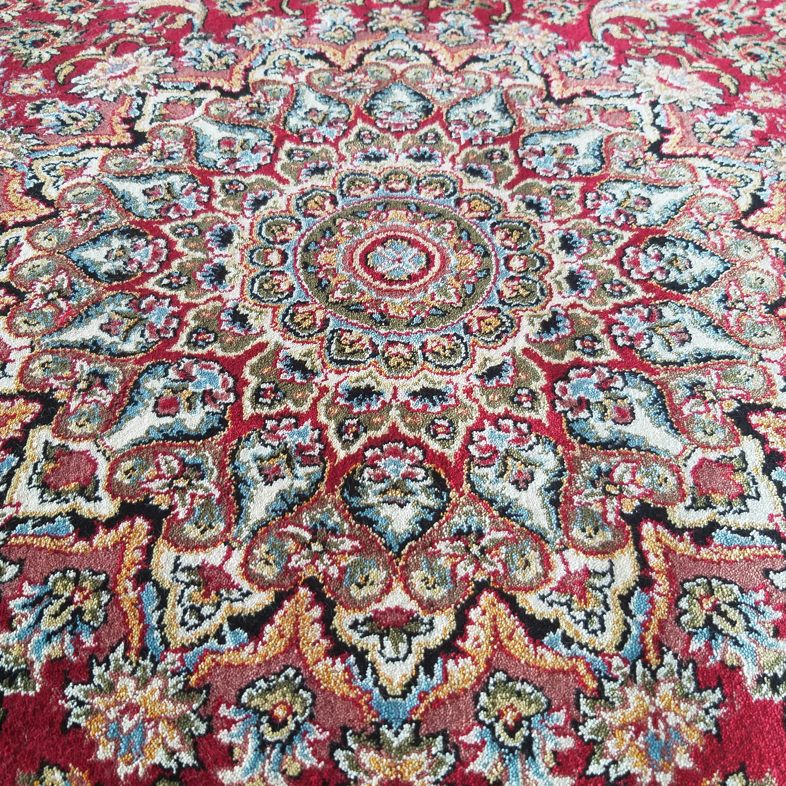 Tapis rouge orné de motifs complexes traditionnels : médaillon central, fleurs et formes paisley en bleu, or, blanc, vert et noir