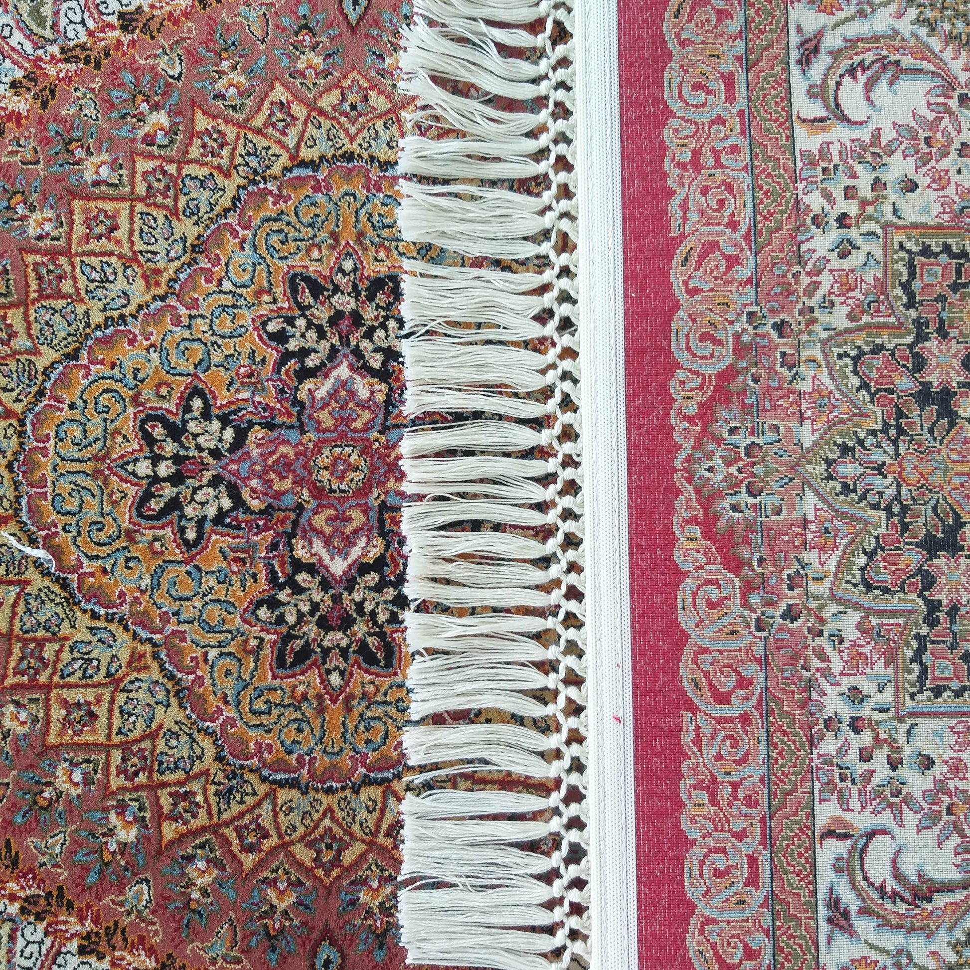 Tapis aux motifs floraux et arabesques complexes, dont les sections rouge et crème sont séparées par des franges blanches