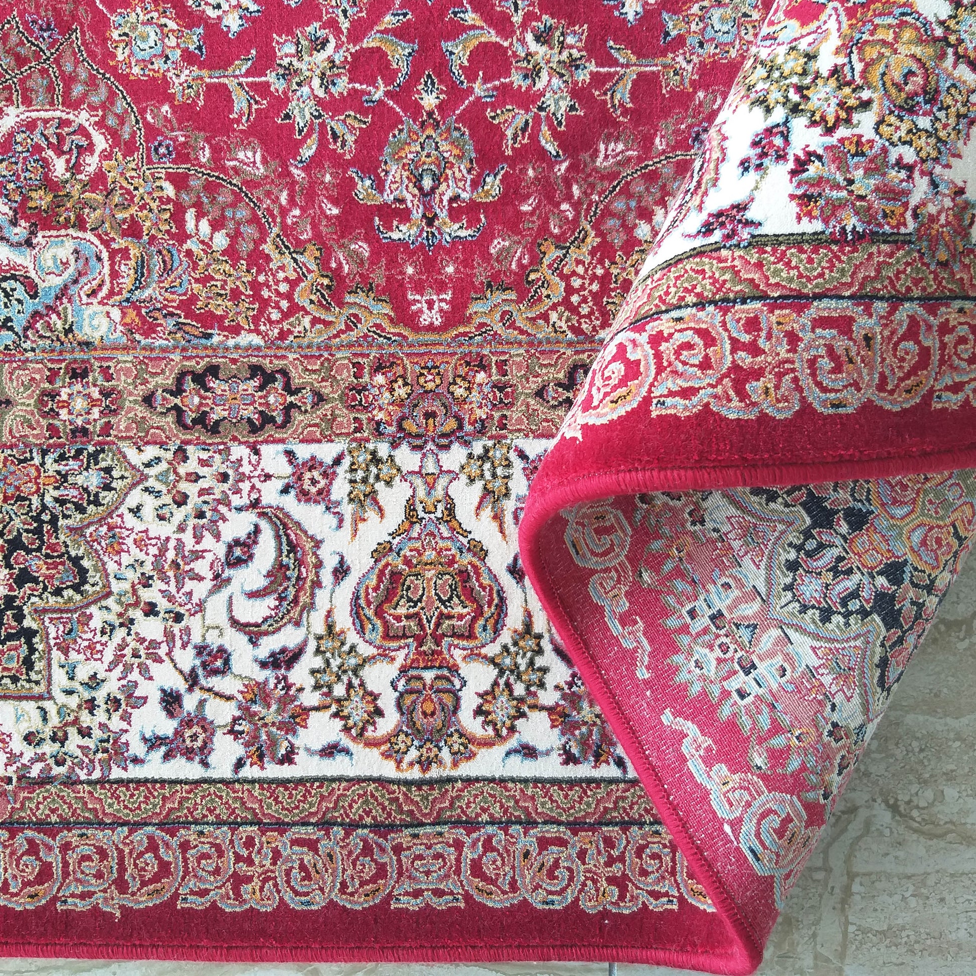 Tapis à riches motifs floraux orientaux rouges et blancs, une partie est enroulée, montrant sa texture tissée