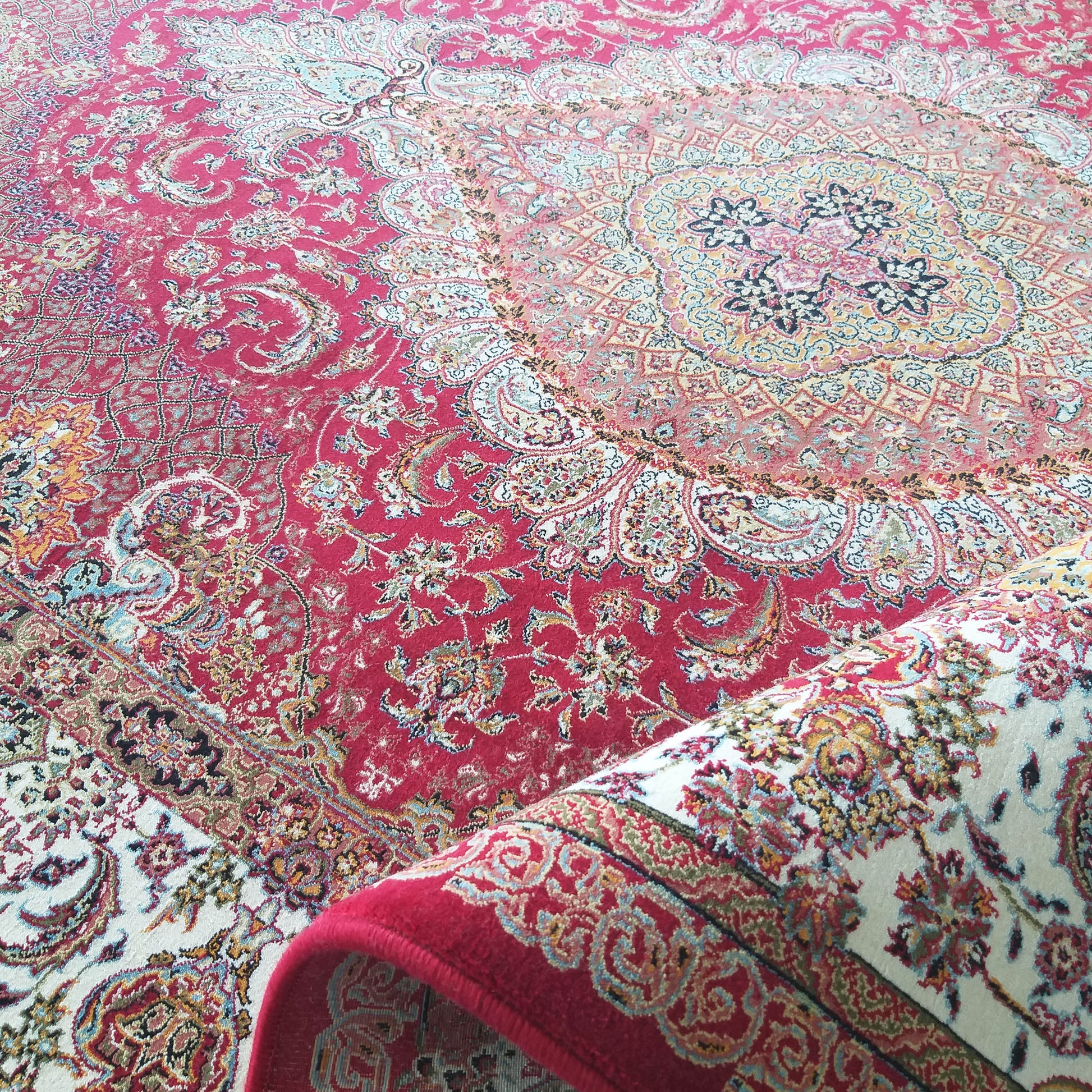 Tapis rouge vif avec de riches motifs floraux et un médaillon central coloré, dont une partie est roulée