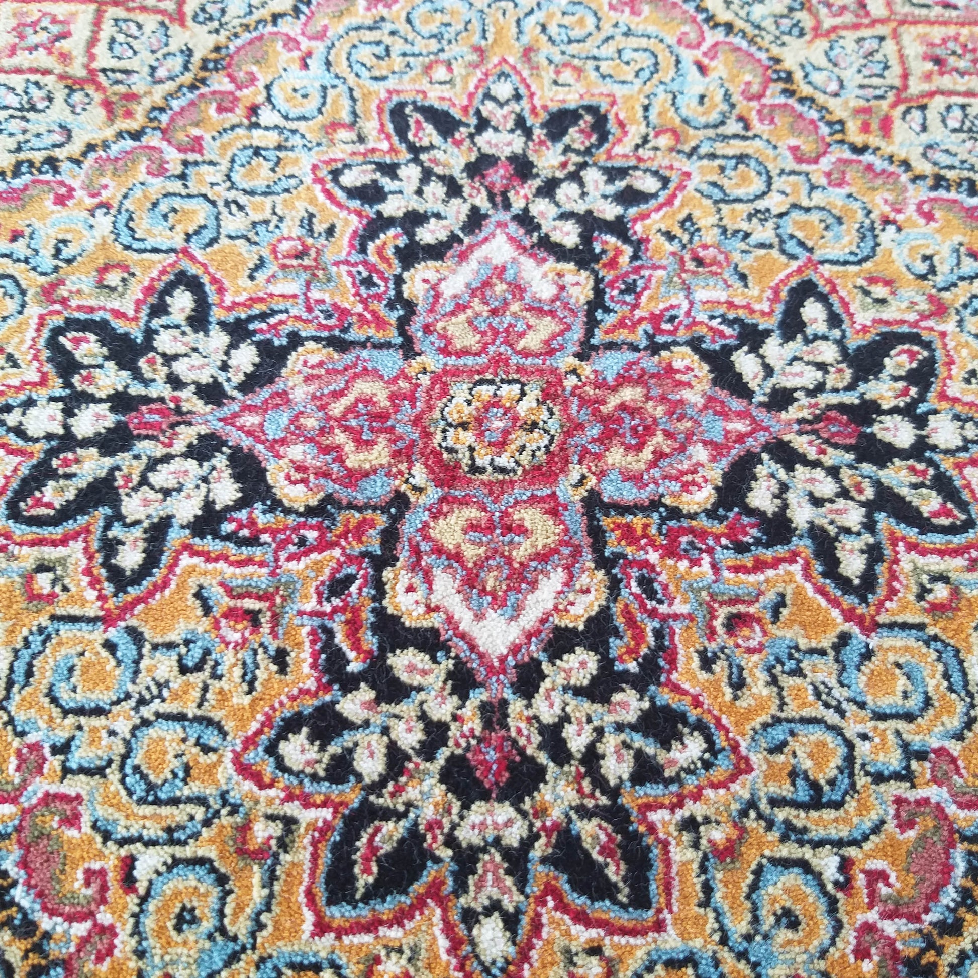 Tapis moelleux aux motifs orientaux symétriques, richement coloré en rouge, noir, doré, bleu et crème