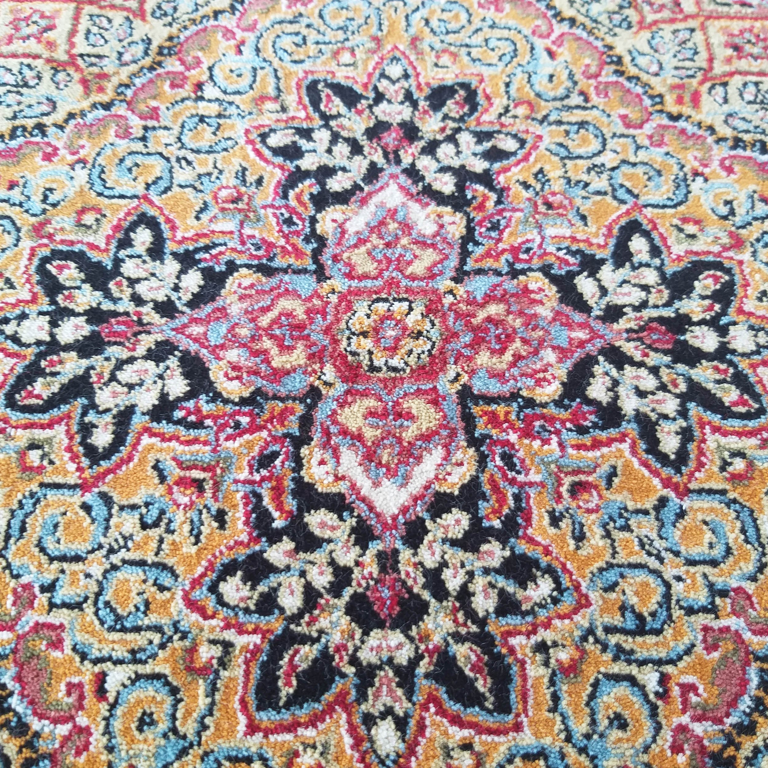 Tapis moelleux aux motifs orientaux symétriques, richement coloré en rouge, noir, doré, bleu et crème